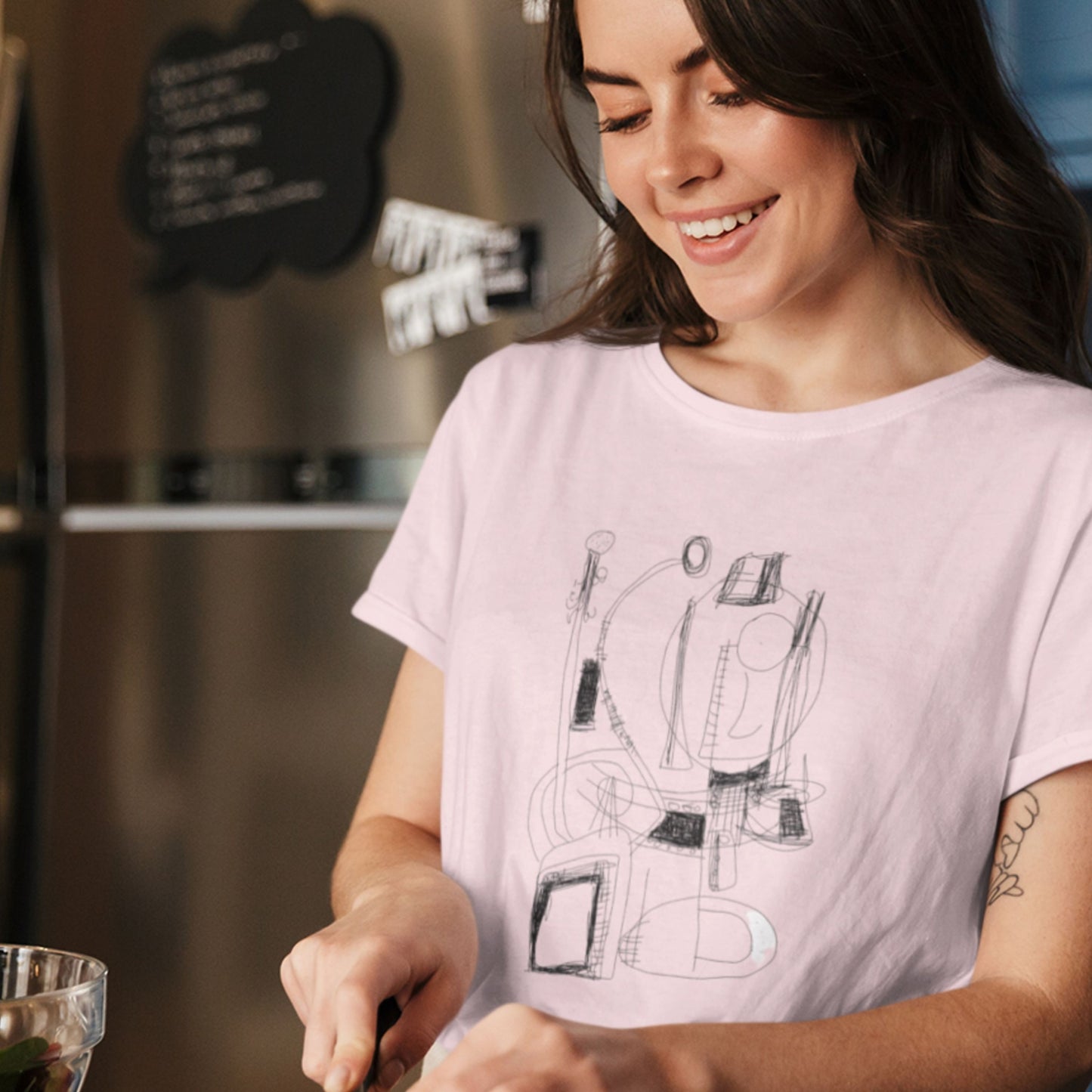 Woman wearing a light purple t-shirt with a graphic design, standing in a kitchen.