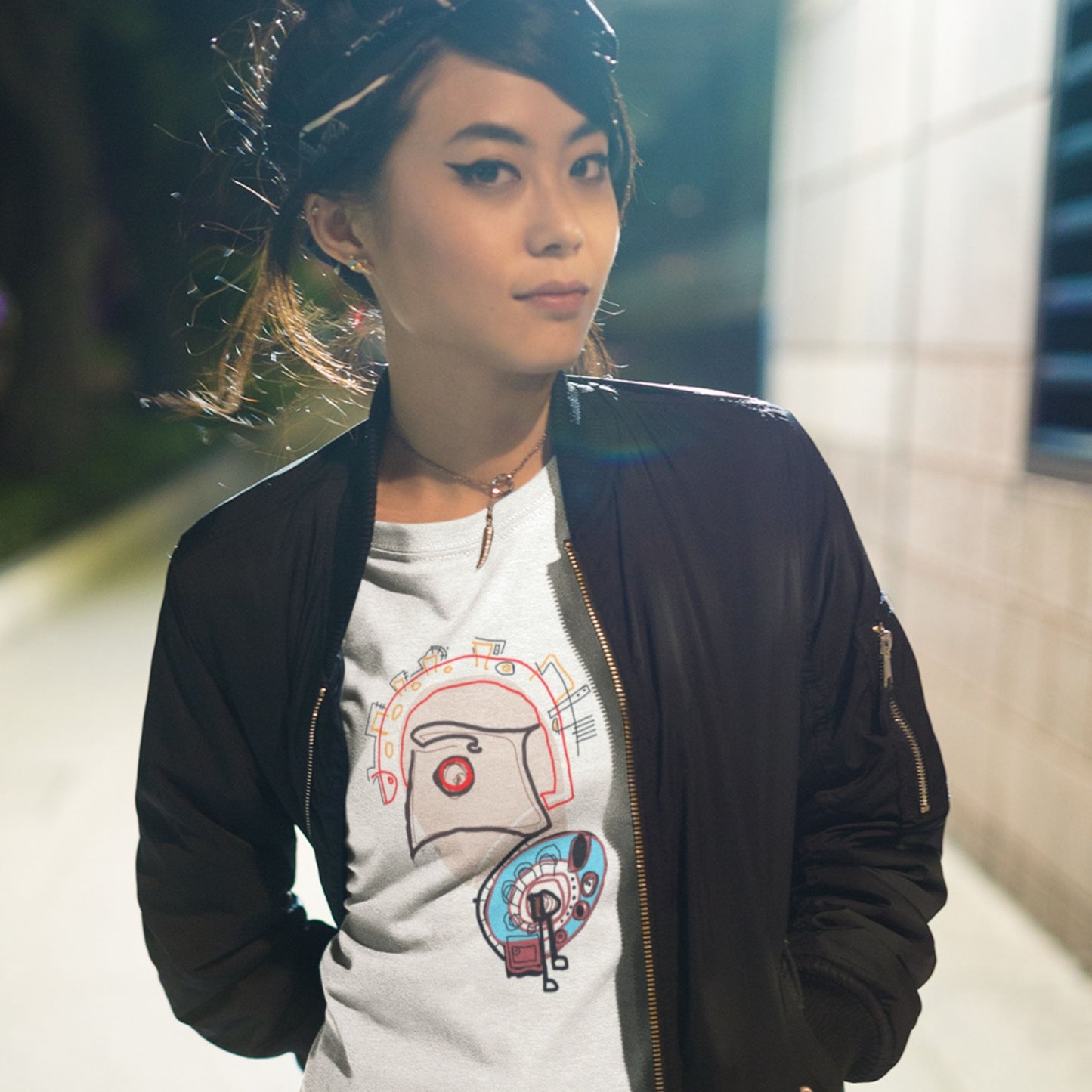 Woman wearing a black jacket and graphic t-shirt in an urban setting.