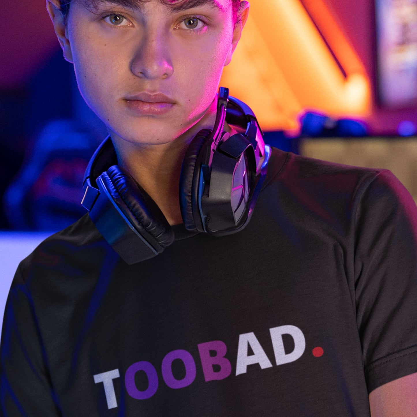 Person wearing a black t-shirt with 'TOOBAD' text, large headphones, in a colorful room.