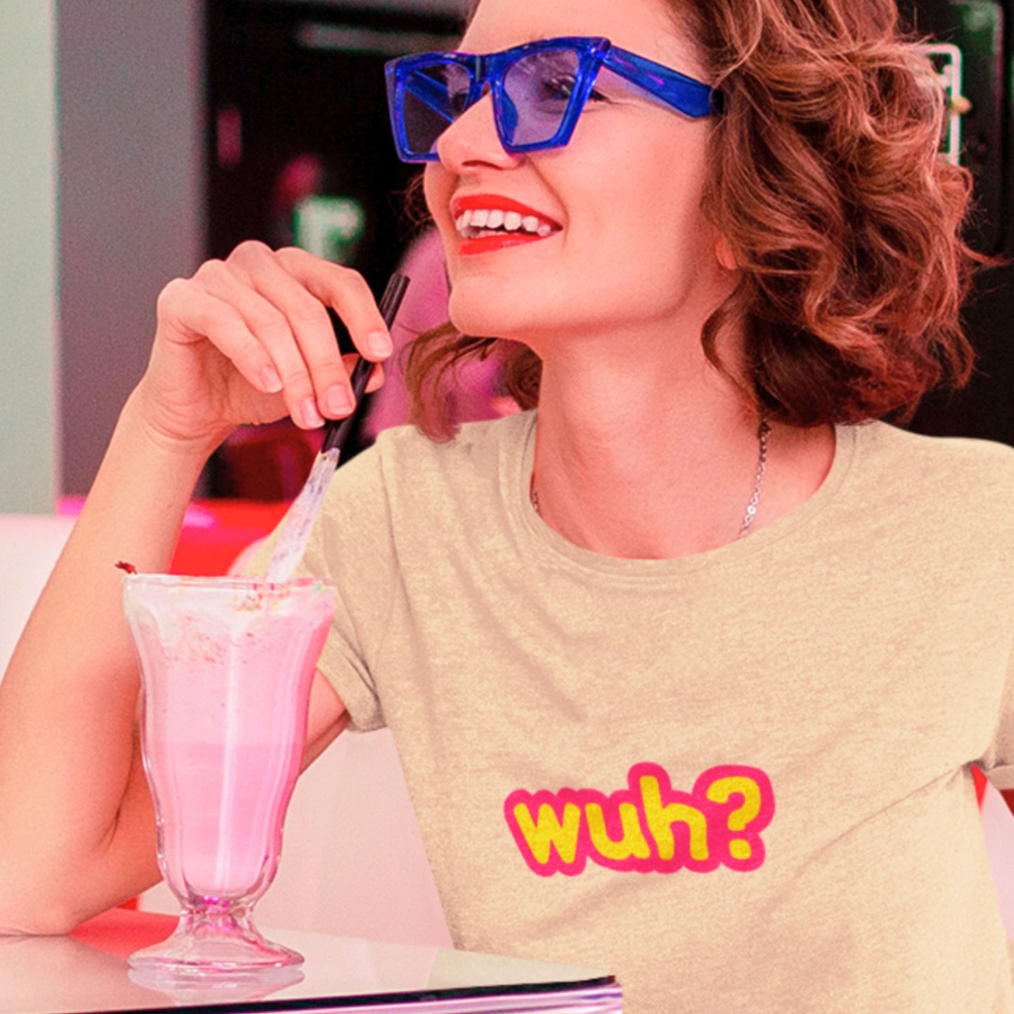 Person wearing a shirt with 'wuh?' text, holding a pink milkshake.