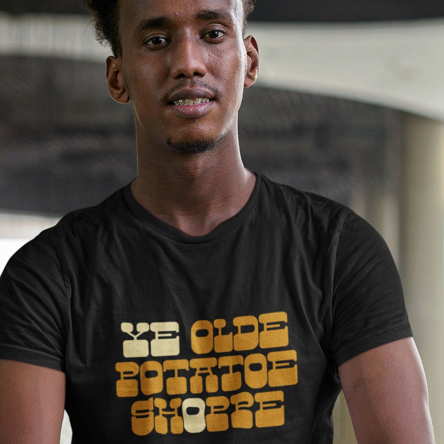 Man wearing a black t-shirt with 'Ye Olde Potato Shoppe' text in yellow.