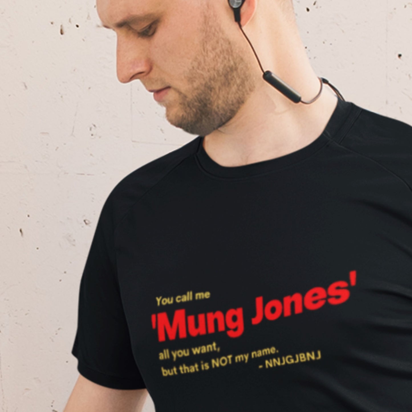 Man wearing a black t-shirt with red and yellow text against a beige wall.