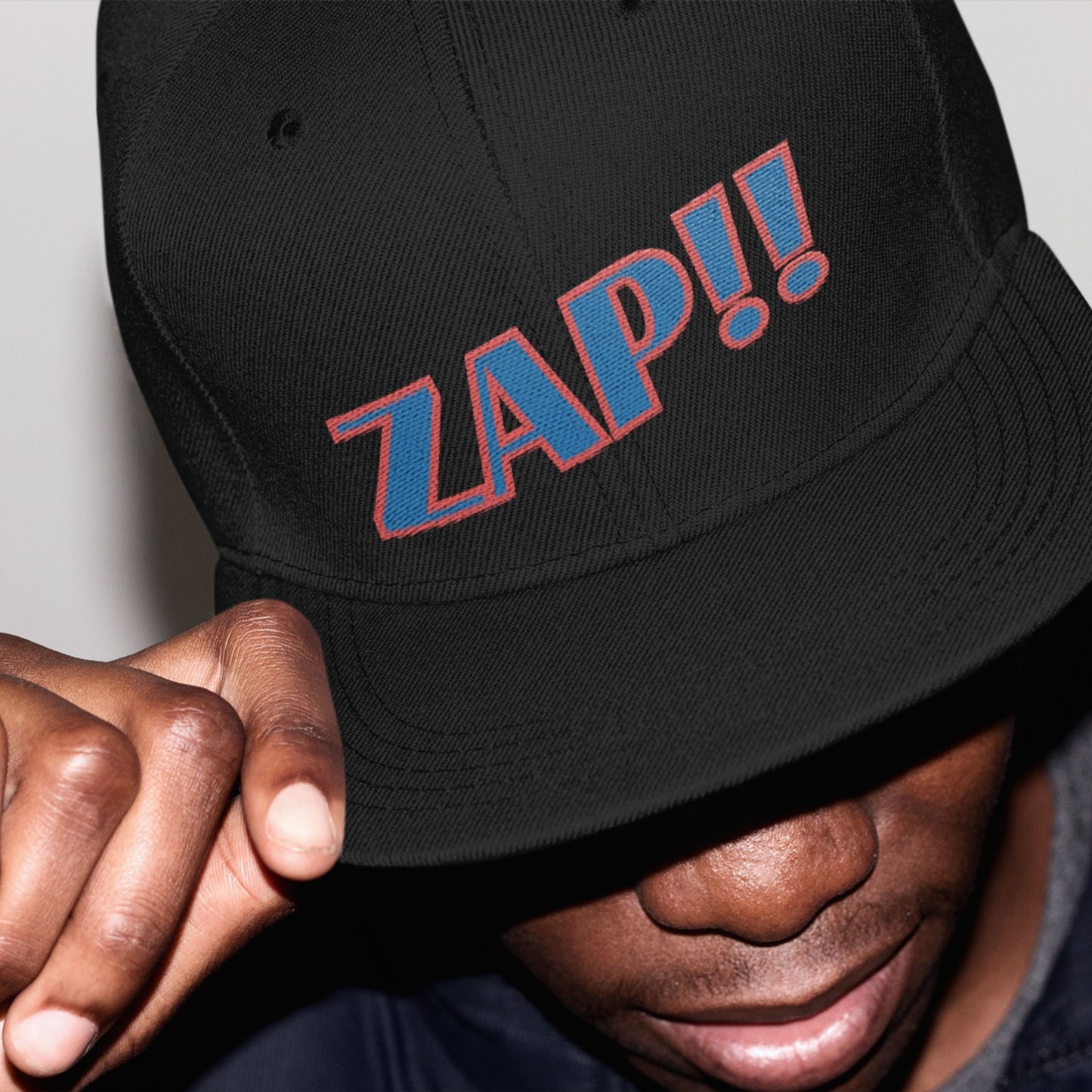 Black cap with 'ZAP!!' text worn by a person, against a neutral background.