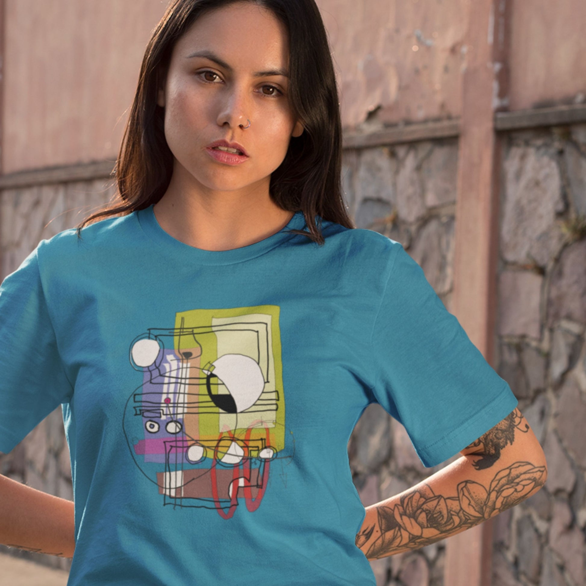 Serious woman wearing an aqua blue t-shirt with a colorful abstract system diagram drawing outside.