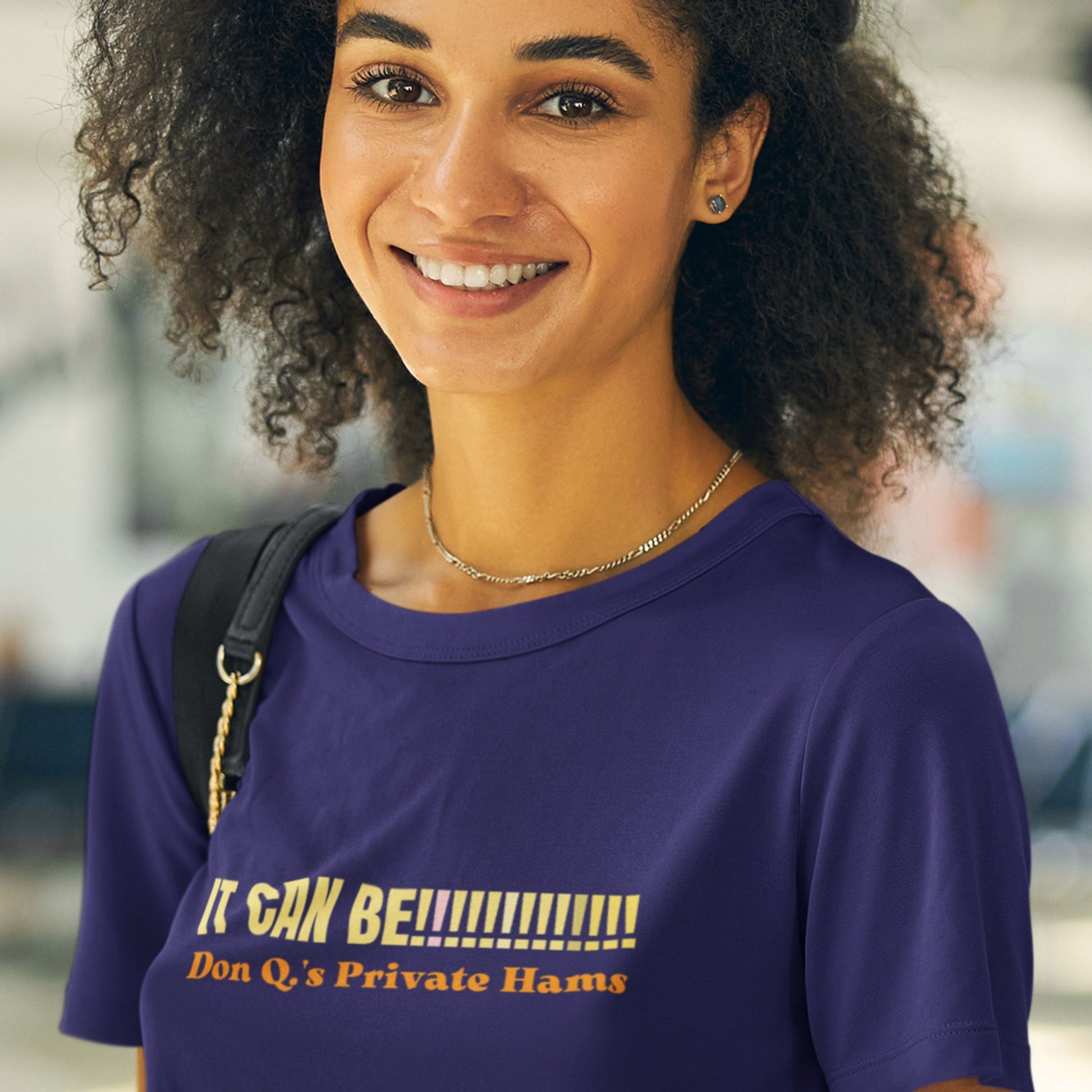 Woman wearing a purple t-shirt with humorous text, standing outdoors.