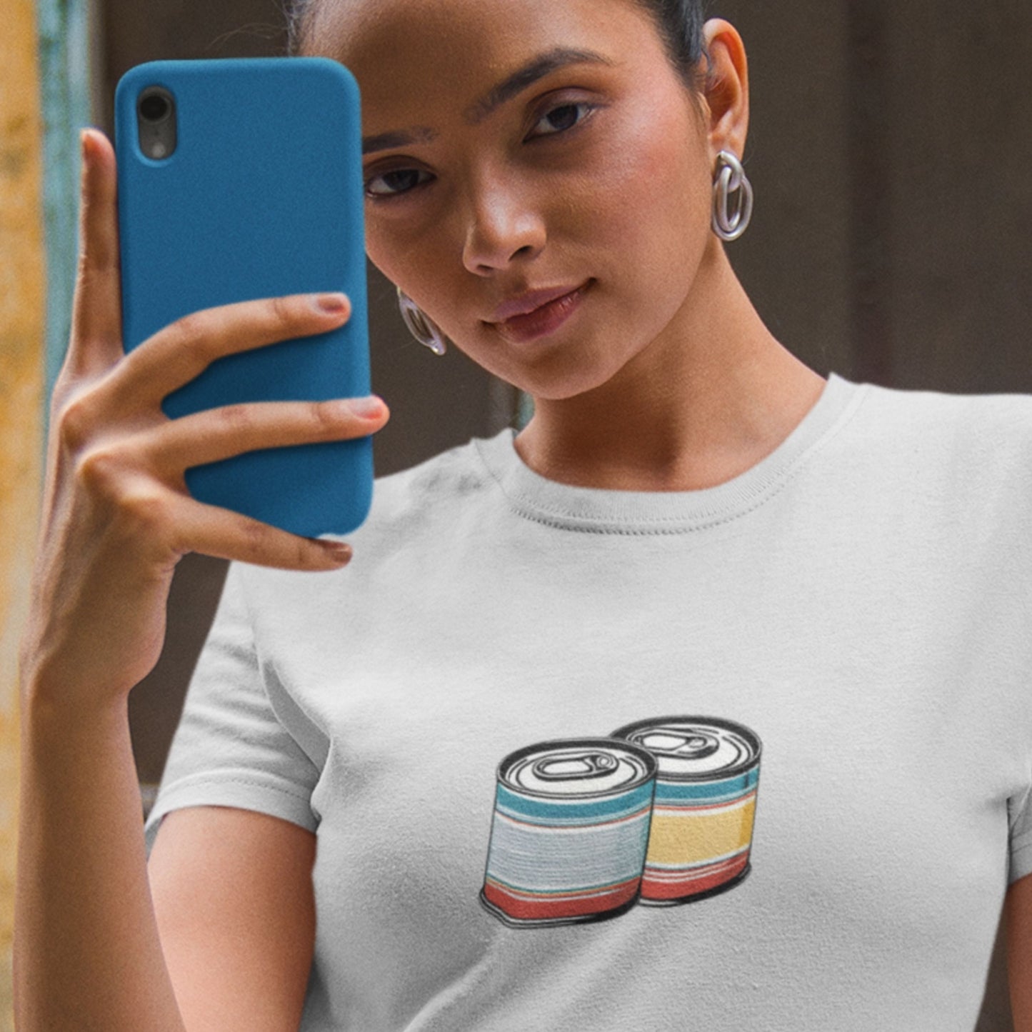 Woman wearing a gray t-shirt with colorful can designs, holding a blue phone.