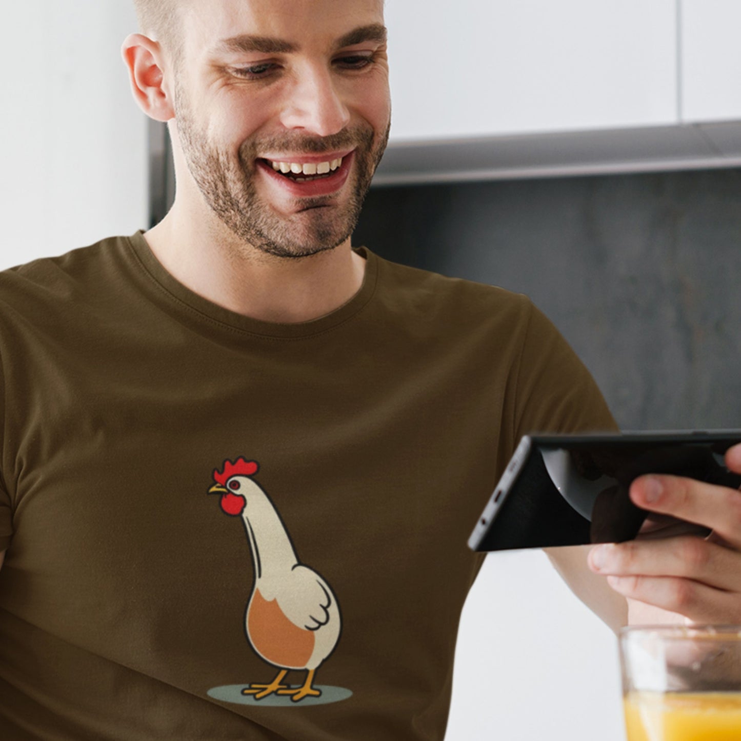 Guy on his phone smiling and wearing a brown t-shirt with a simple cartoon illustration of a chicken.