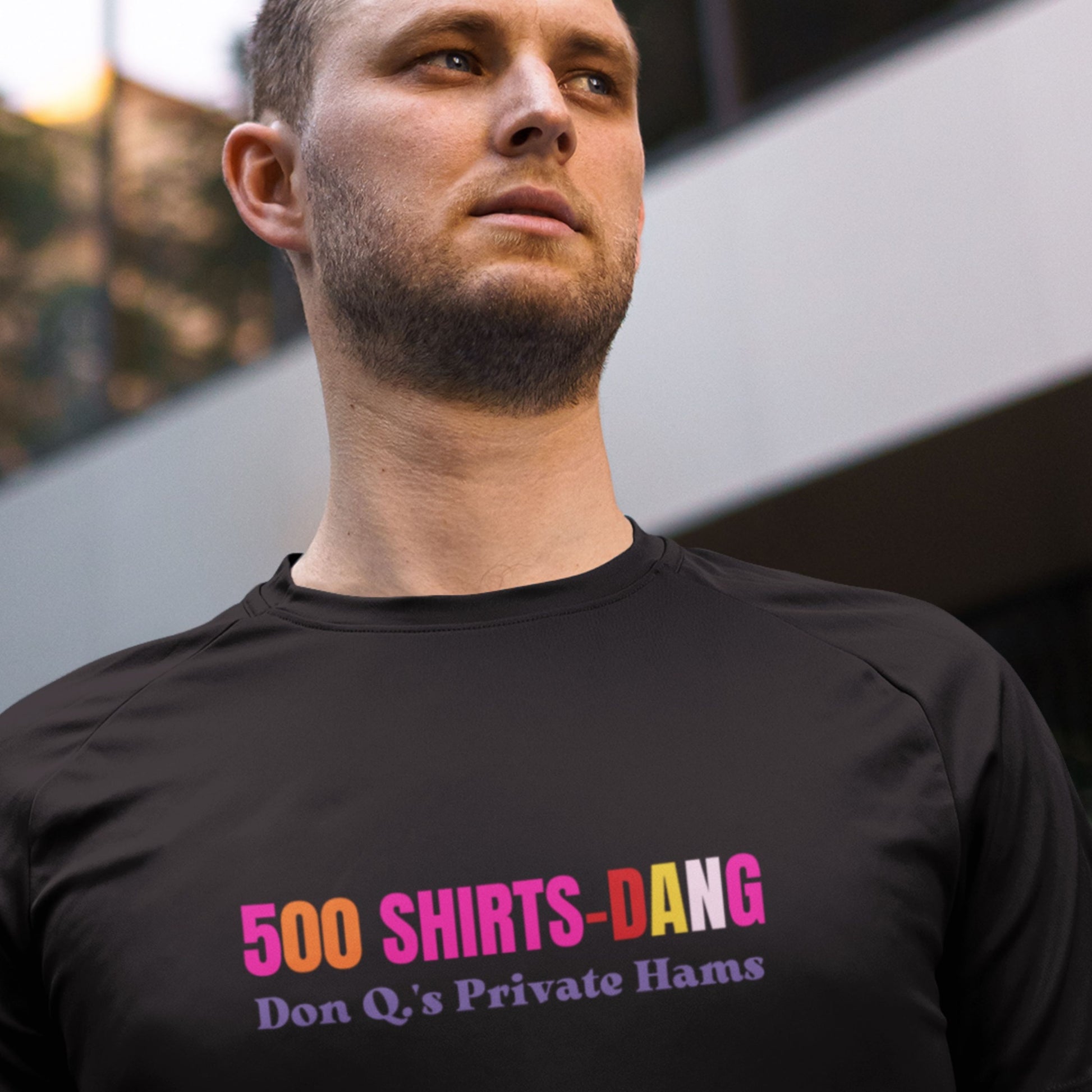 Man wearing a black t-shirt with humorous colorful text in front of a building.