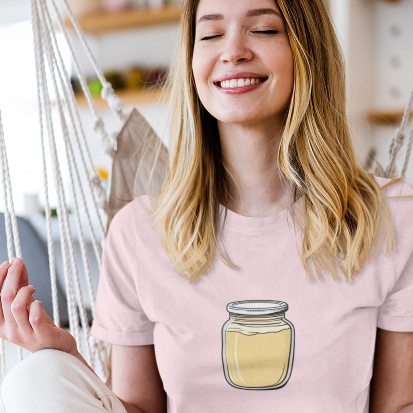 Woman wearing a pink t-shirt with a jar design, sitting in a hammock.