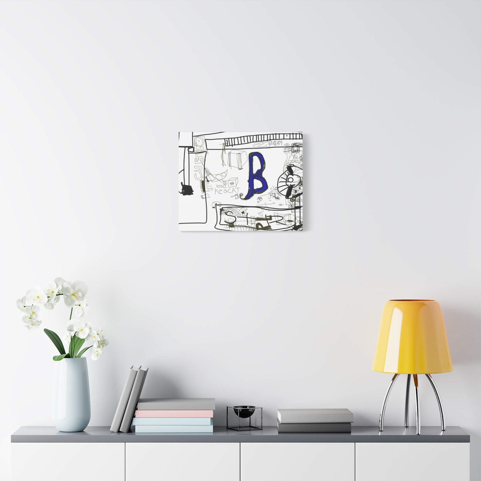 Decorative wall art with a blue letter 'B' on a white wall above a shelf with books and a lamp.