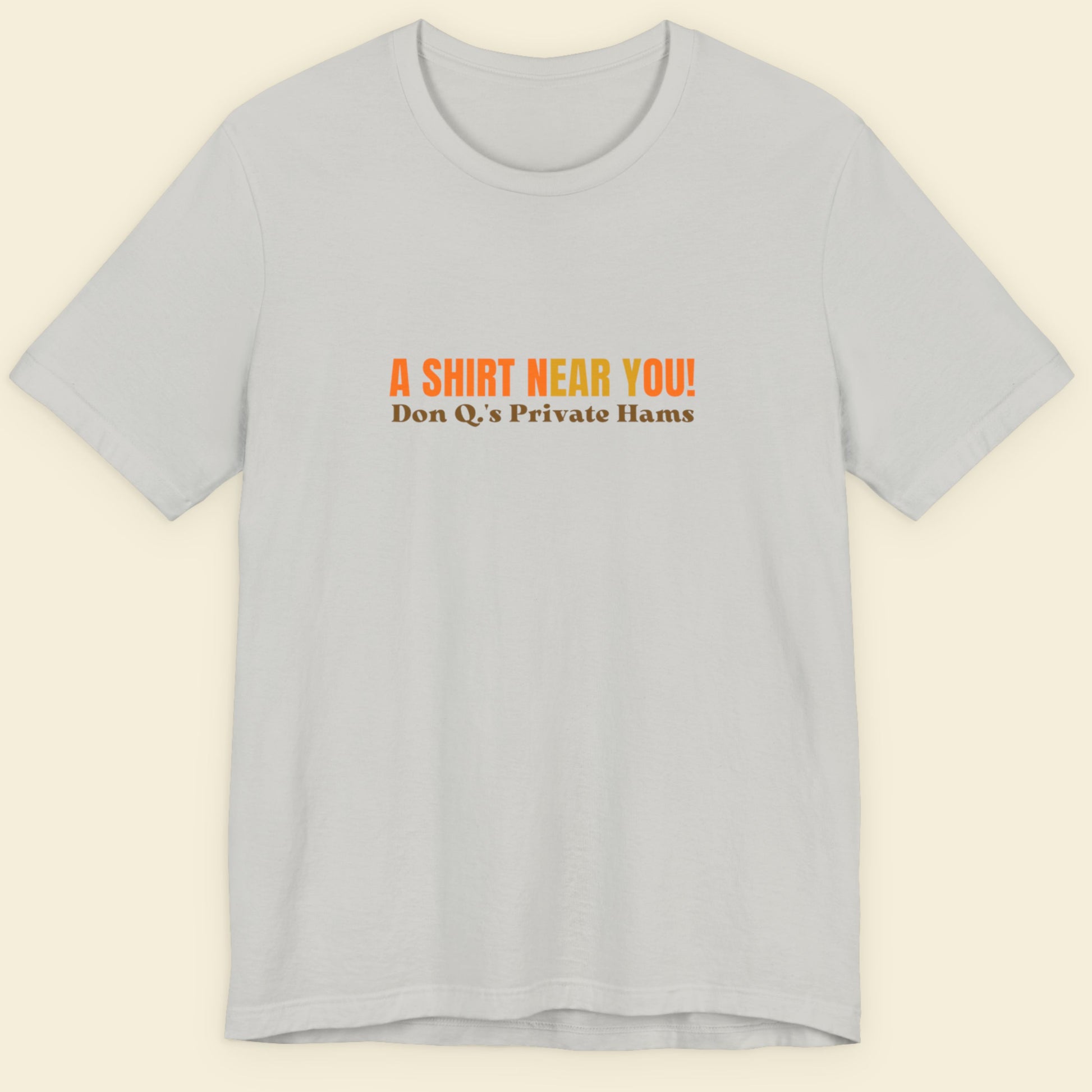 Silver t-shirt with multicolored 'A shirt near you!' text on a beige background.