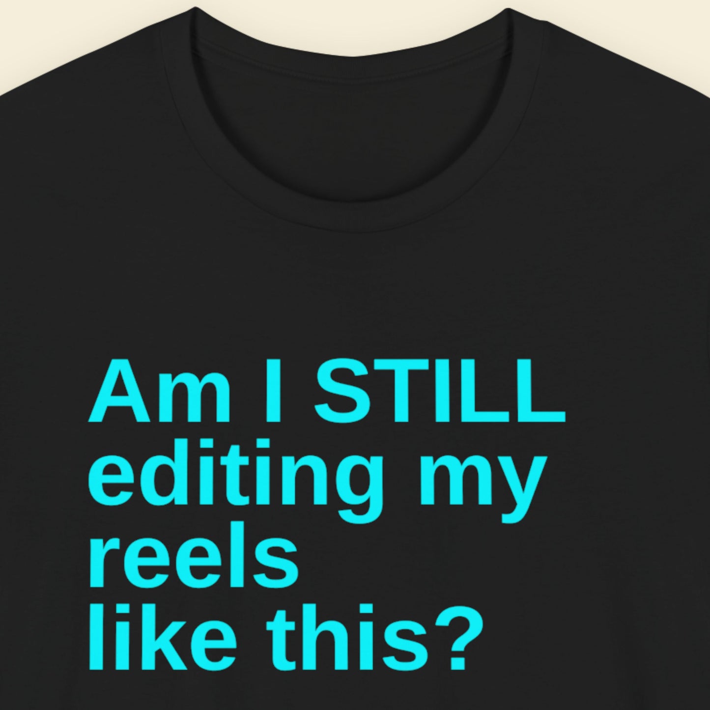 Black t-shirt with blue text 'Am I STILL editing my reels like this?' on a beige background.