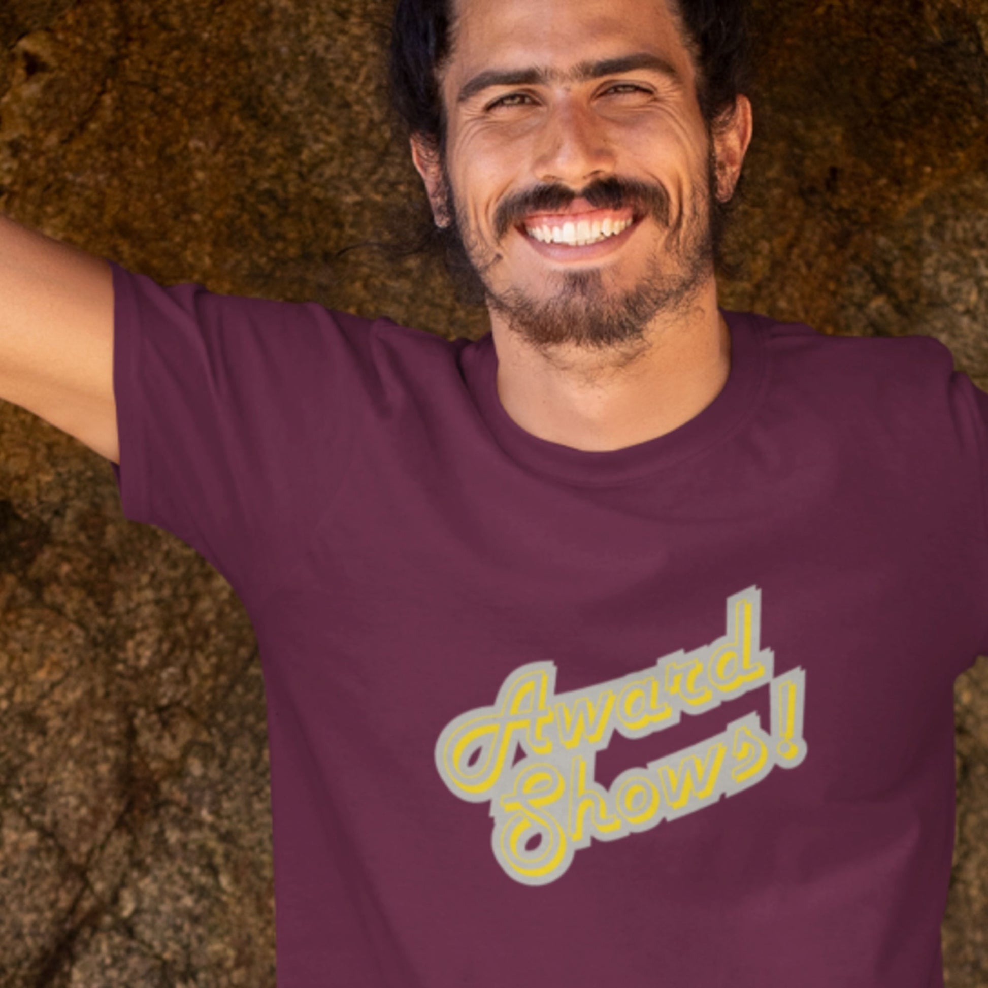 Smiling man wearing a maroon t-shirt with yellow and grey stylized text in a cave.