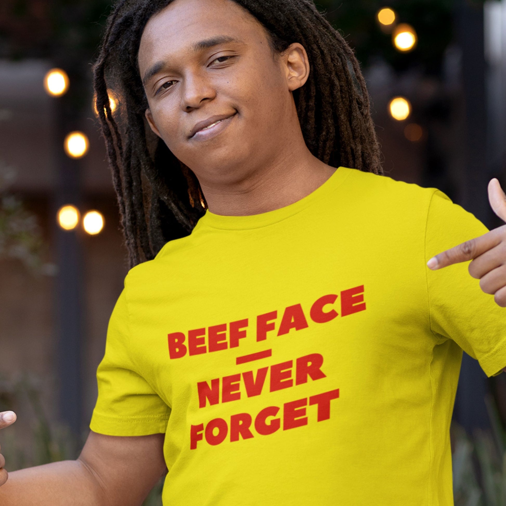 Person wearing a yellow t-shirt with red text 'BEEF FACE NEVER FORGET' pointing to the shirt.