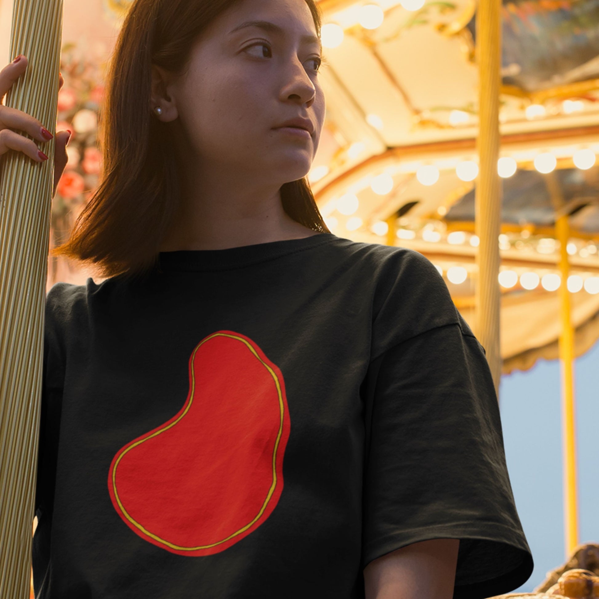 Woman wearing a black t-shirt with a colorful abstract drawing on carousel at night.
