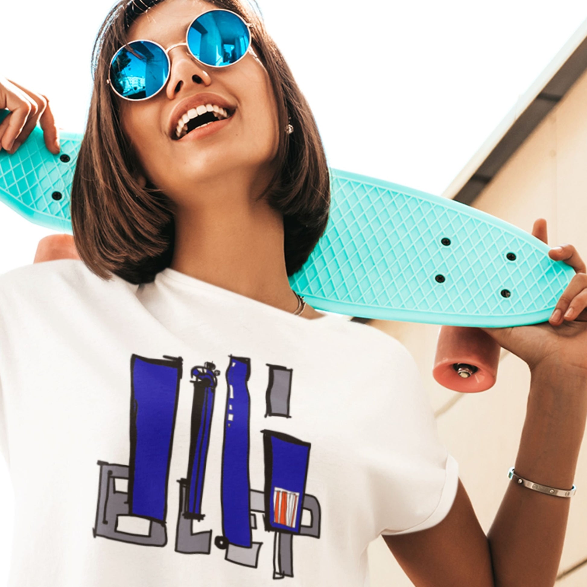 Woman holding a turquoise skateboard with a white t-shirt featuring blue and gray graphics.