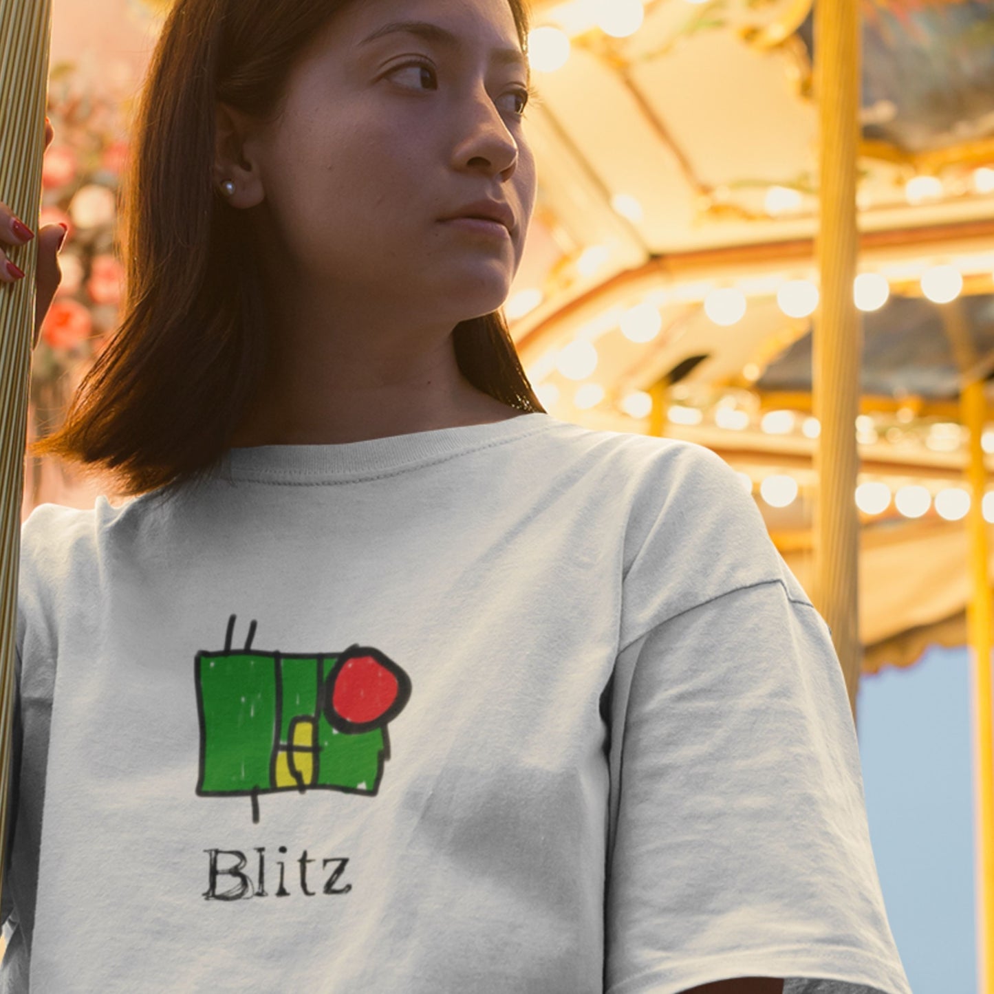 Person wearing a white t-shirt with a colorful design and 'Blitz' text, standing in front of a carousel.