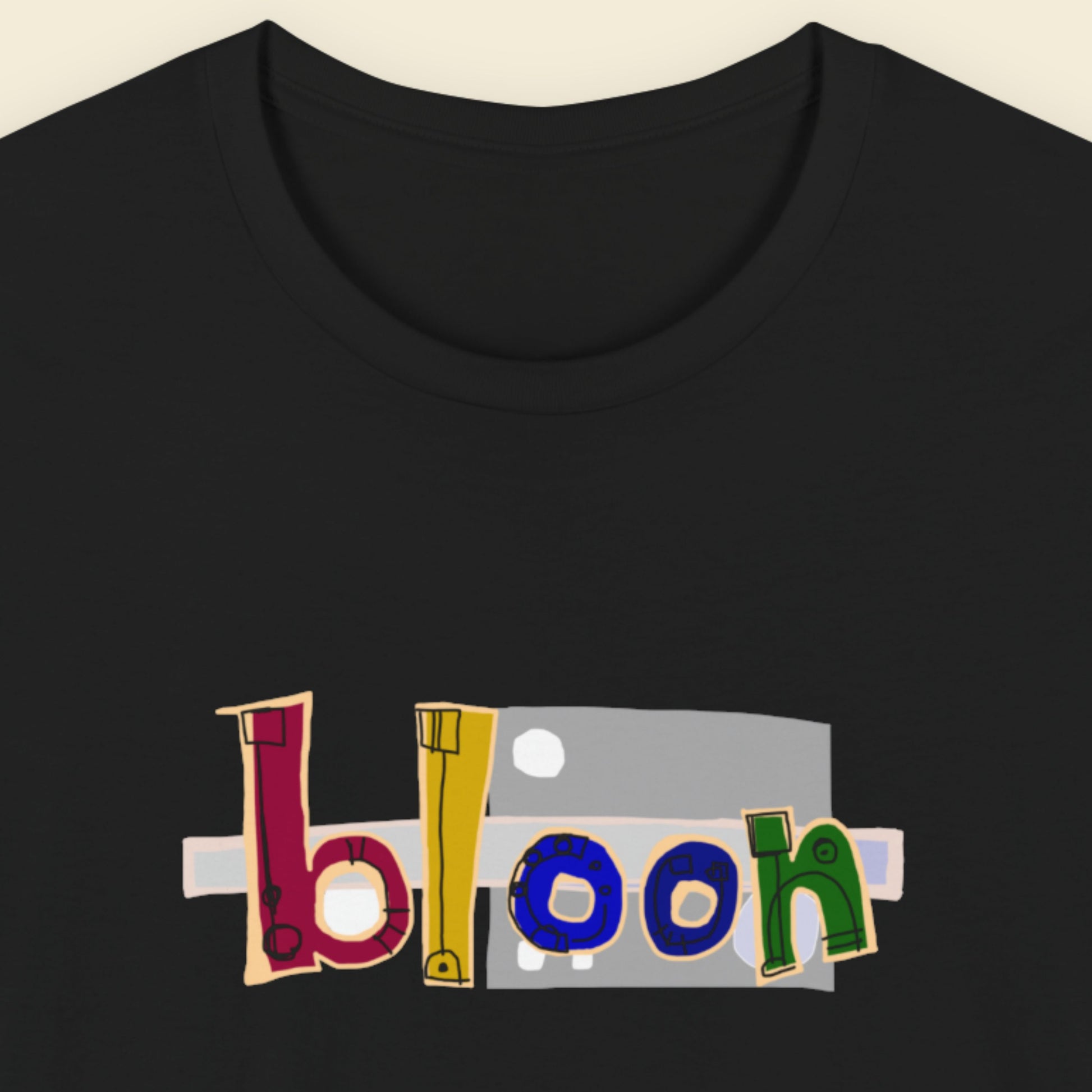 Black t-shirt with a colorful abstract graffiti drawing on a beige background.