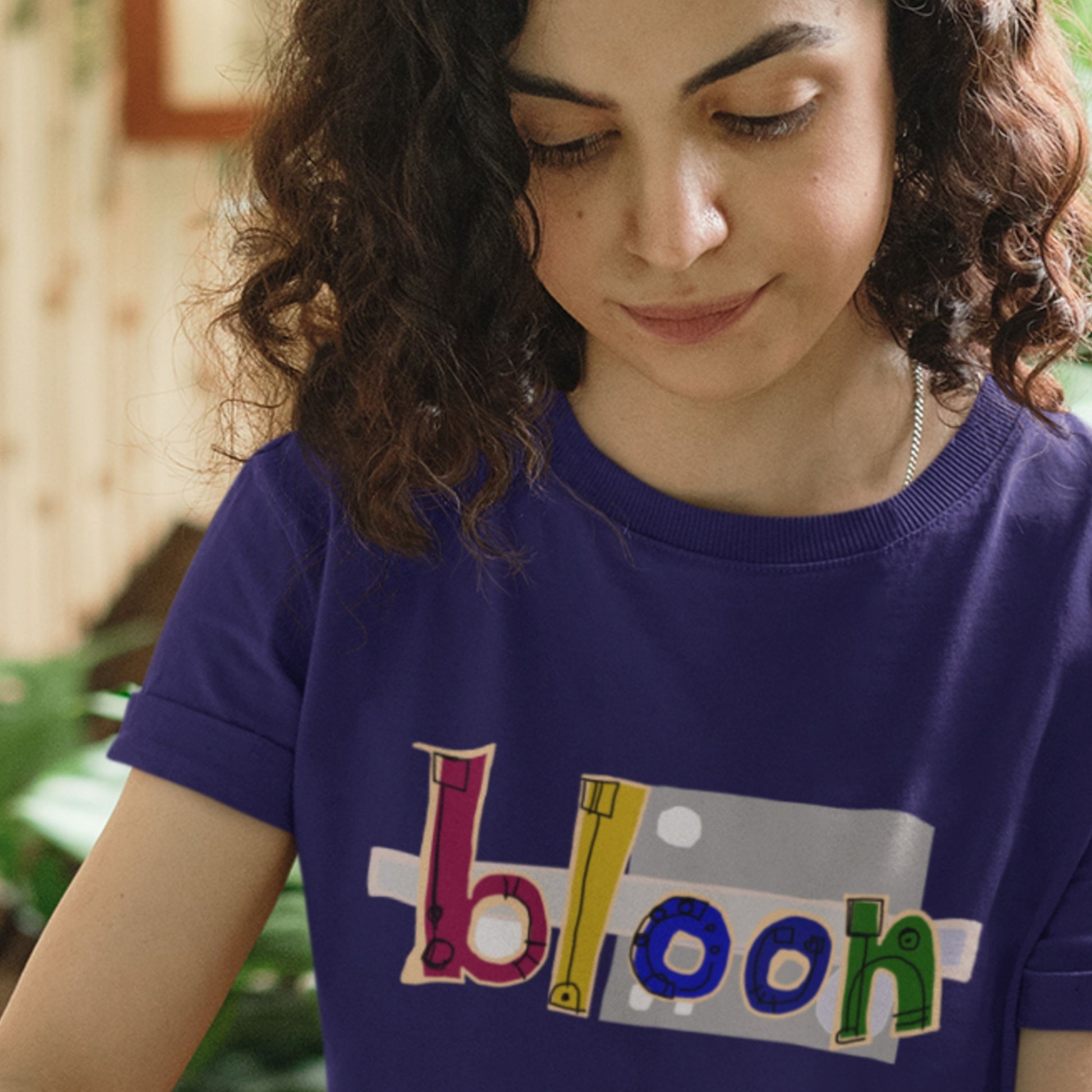 Person wearing a purple t-shirt with 'bloon' printed on it, outdoors.