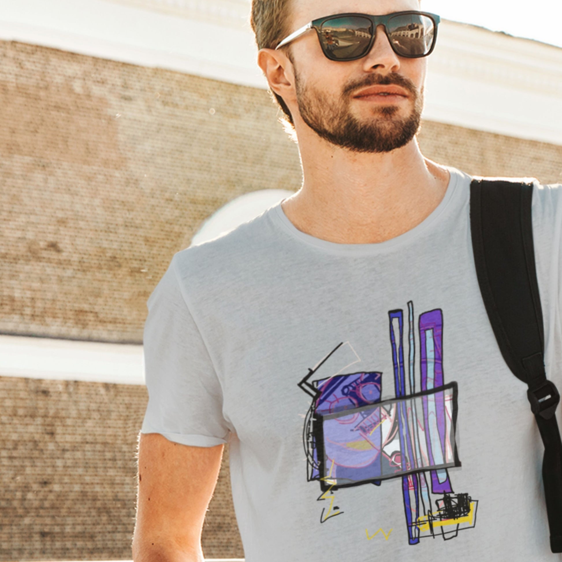 Man wearing a gray t-shirt with a colorful graphic design, standing outdoors.