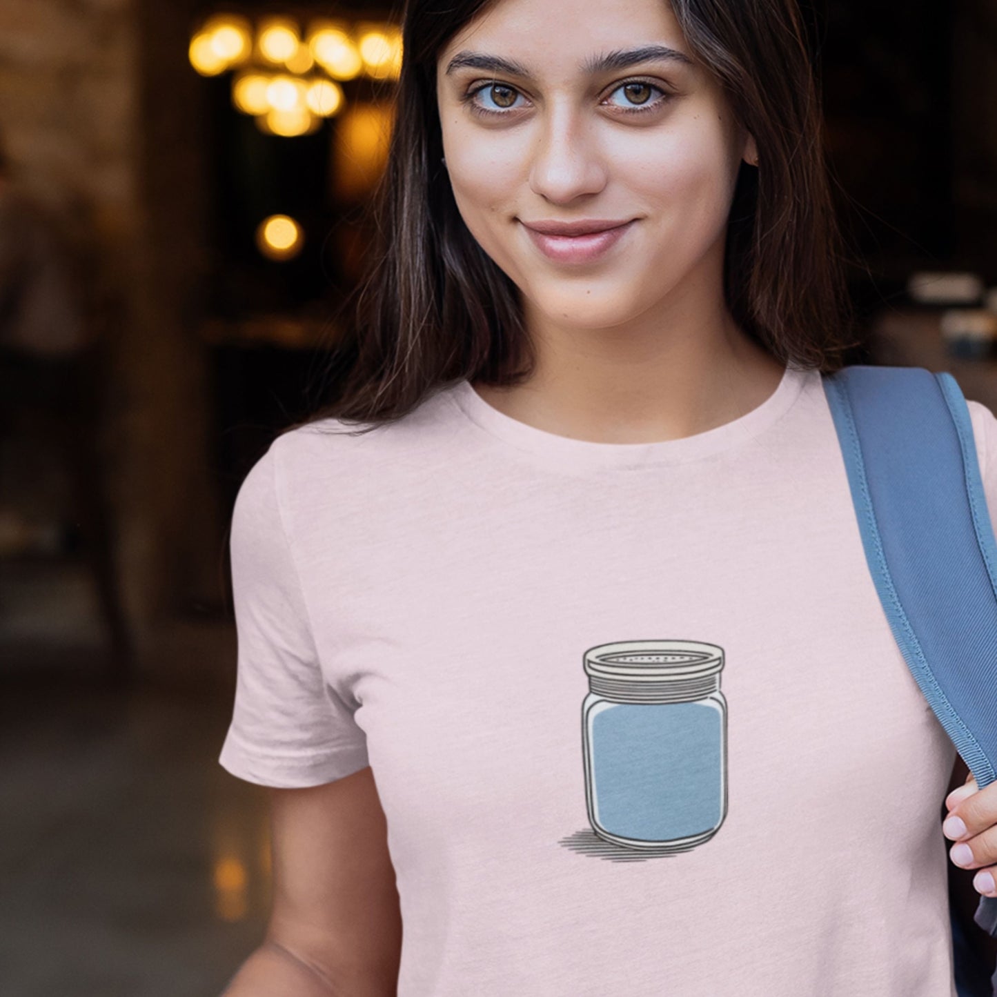 Woman wearing a pink shirt with a drawing of a blue shaker jar in a restaurant.