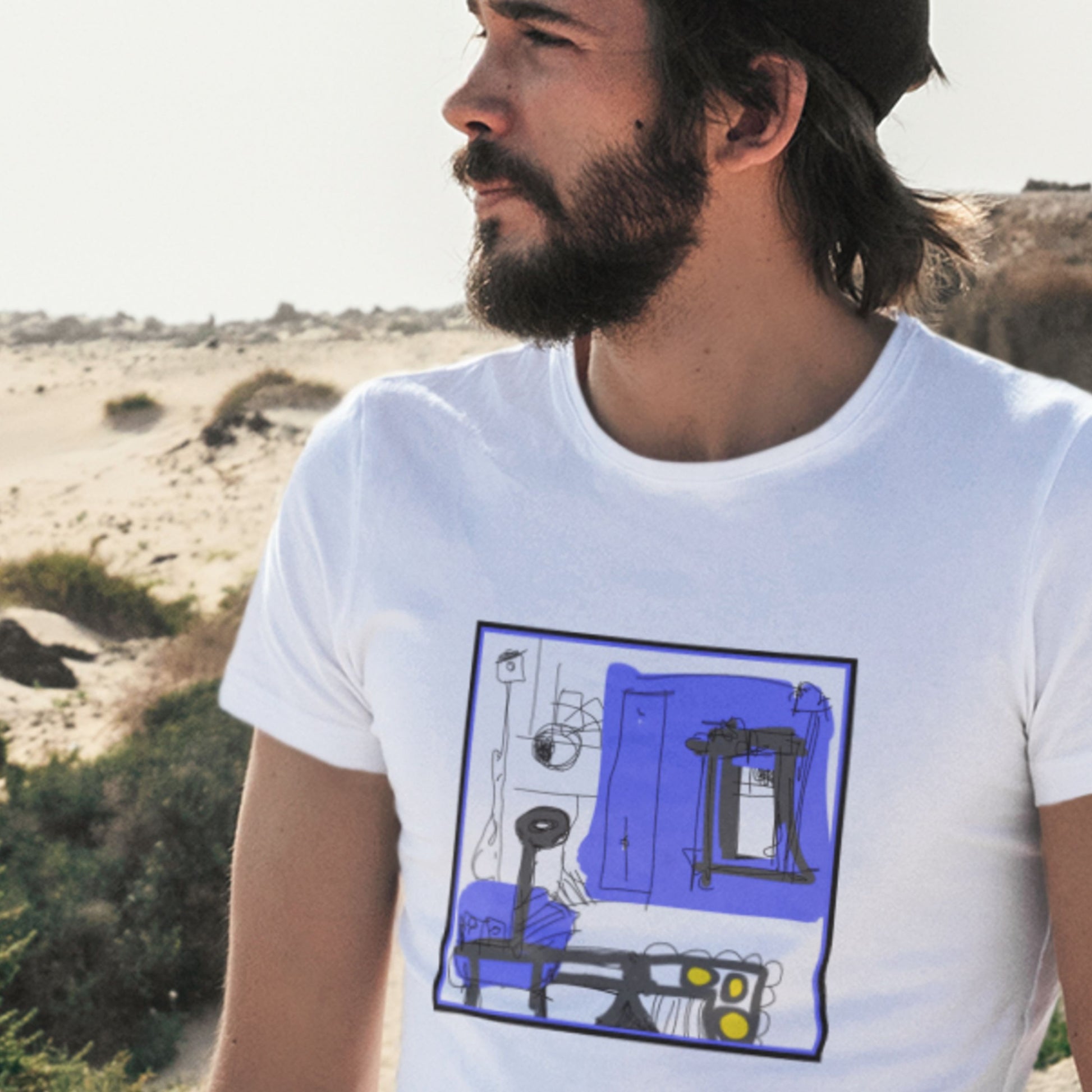 Wistful man wearing a white t-shirt with a colorful abstract drawing on a beach.