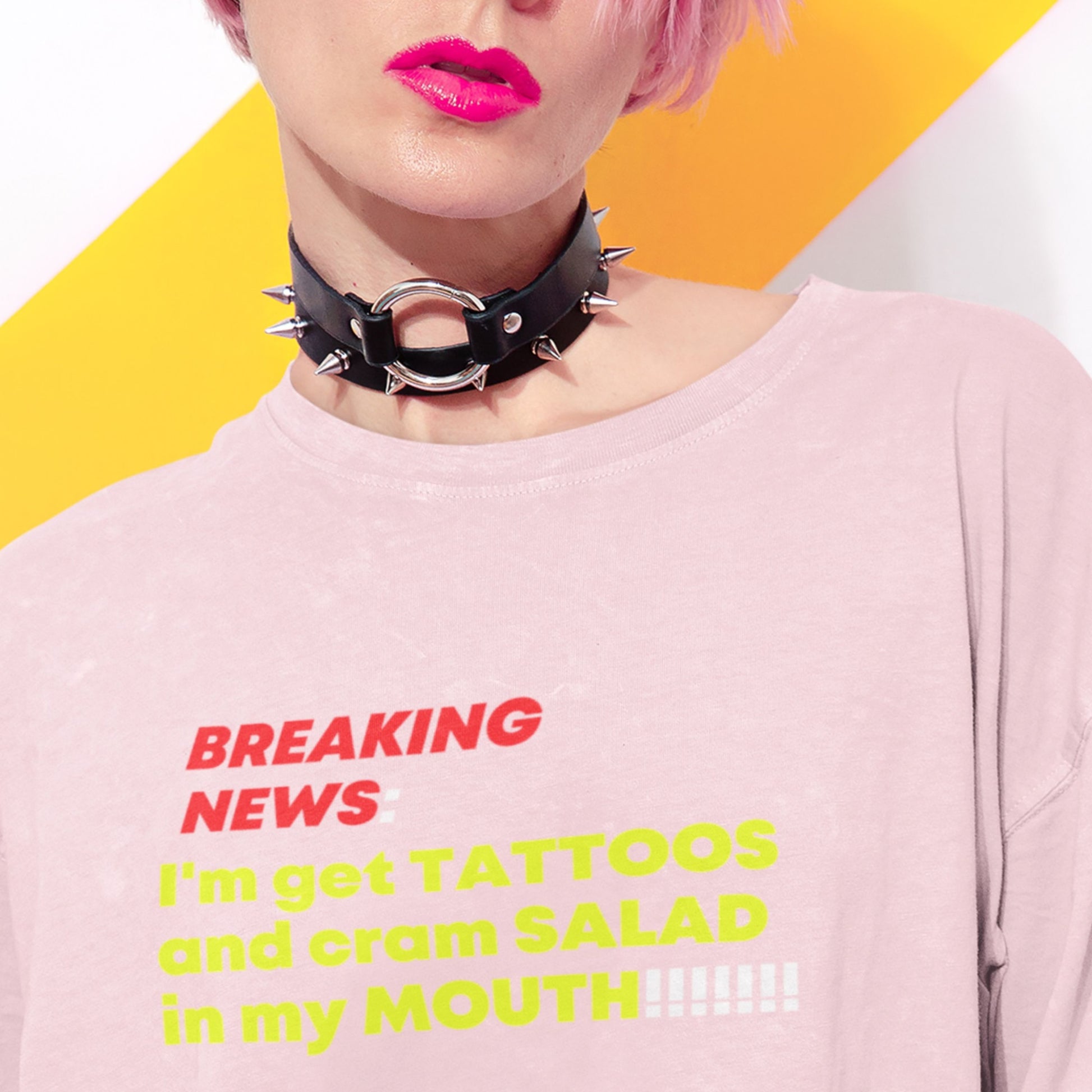Person wearing a pink shirt with humorous text and a black spiked collar against a yellow and white background.