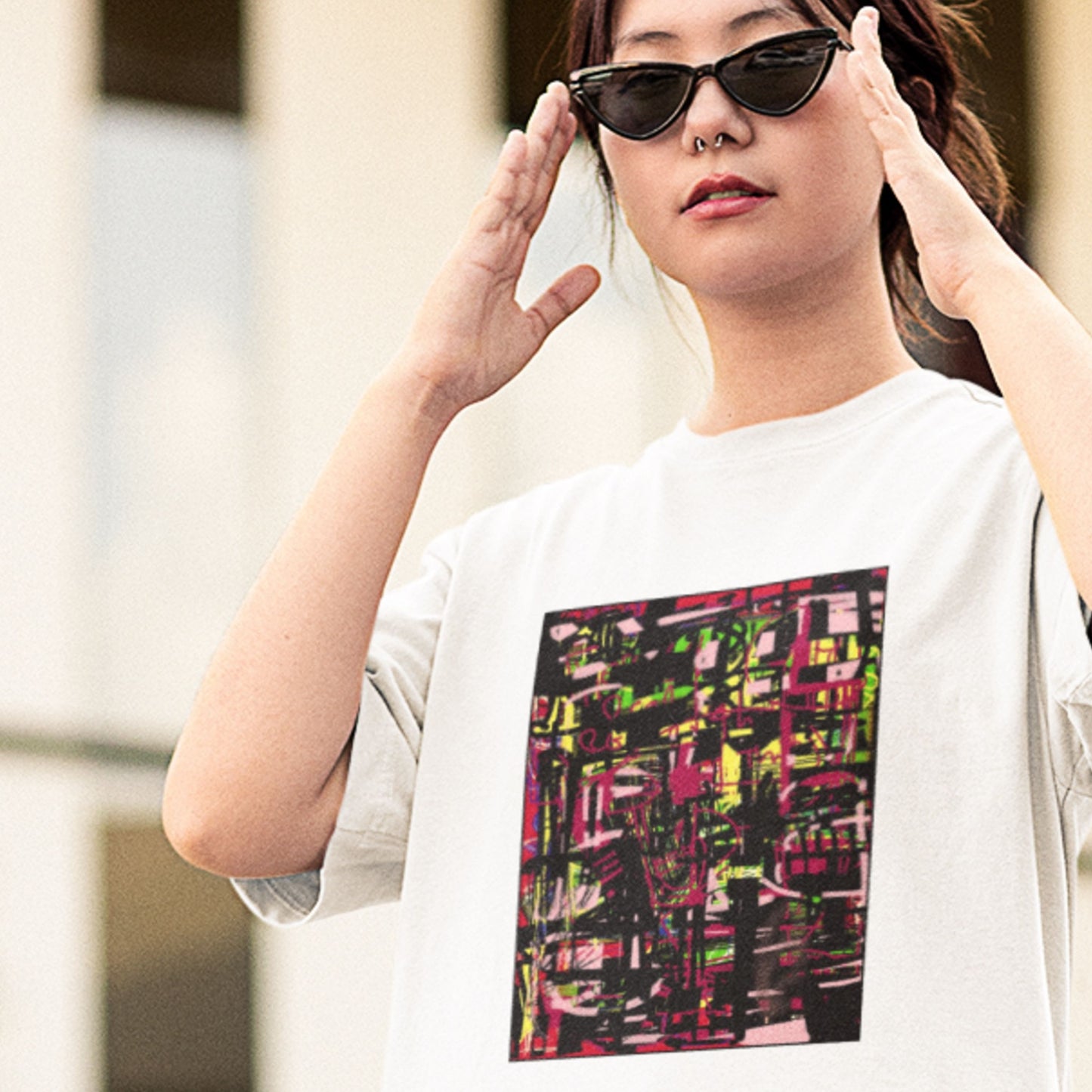 White t-shirt with a colorful abstract drawing worn by a sunglasses wearing woman outside.