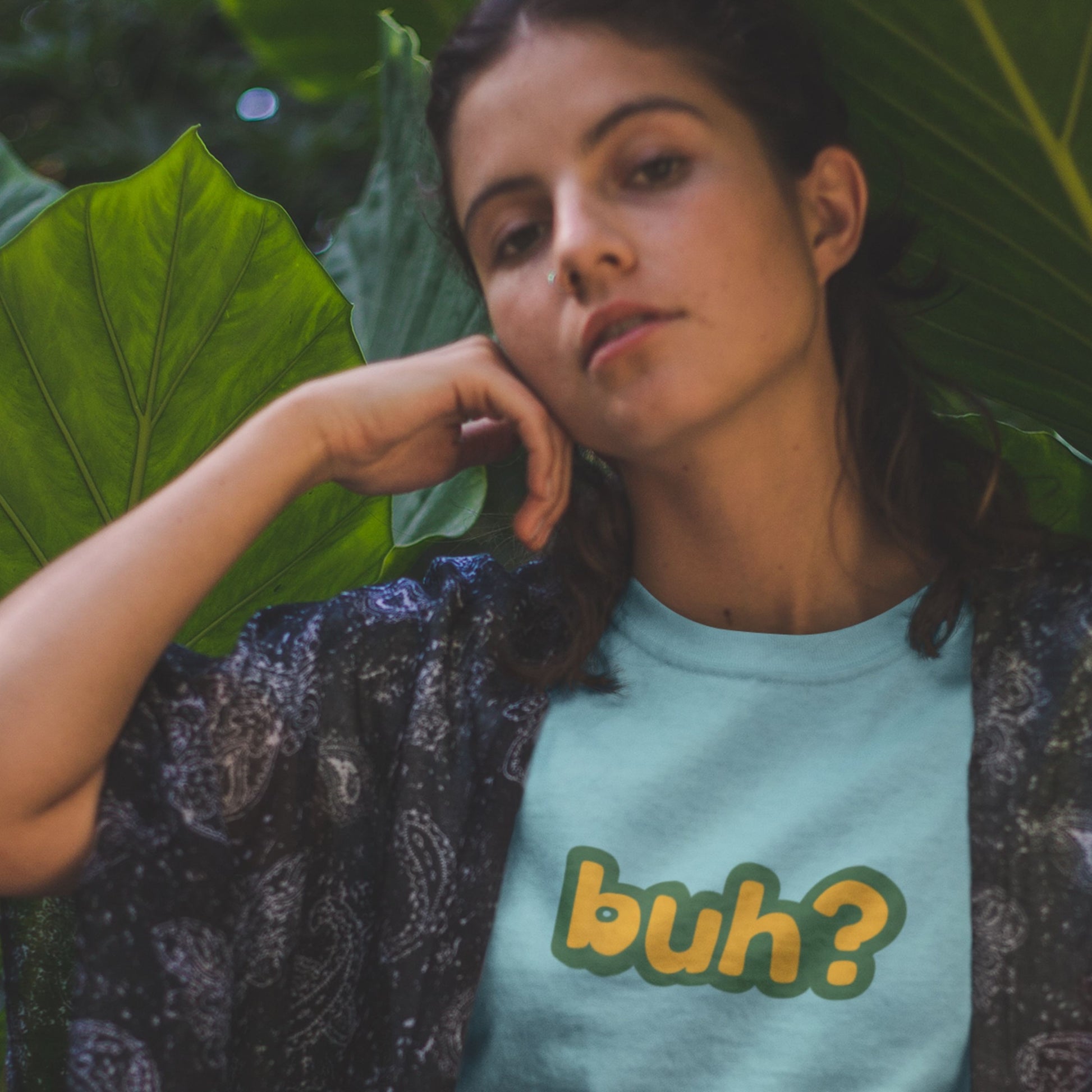 This lady in the plants wearing a turquoise blue t-shirt with multicolored 'buh?' text.