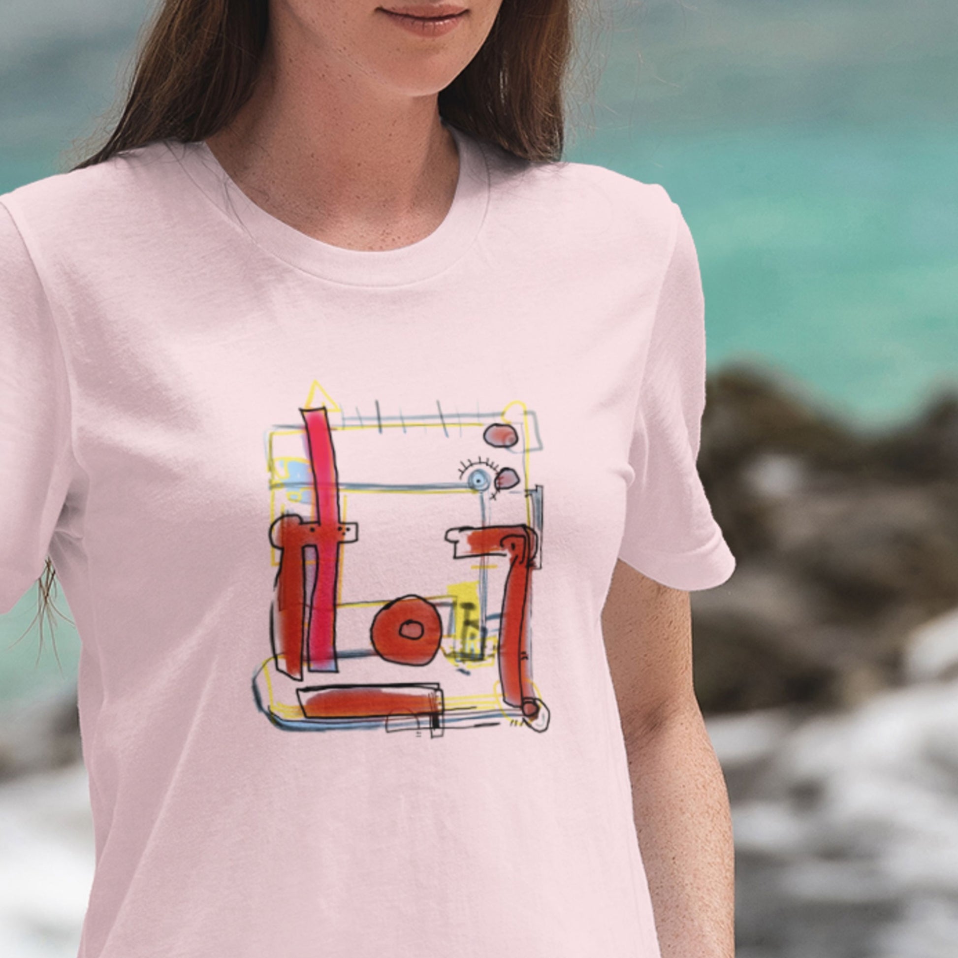Woman wearing a pink t-shirt with a colorful abstract drawing on a beach.