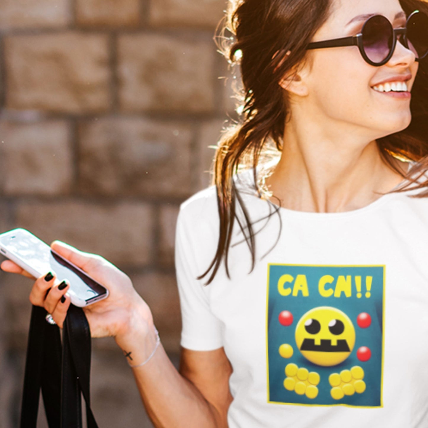 Woman wearing a white t-shirt with a colorful graphic design, holding a phone and a black bag.