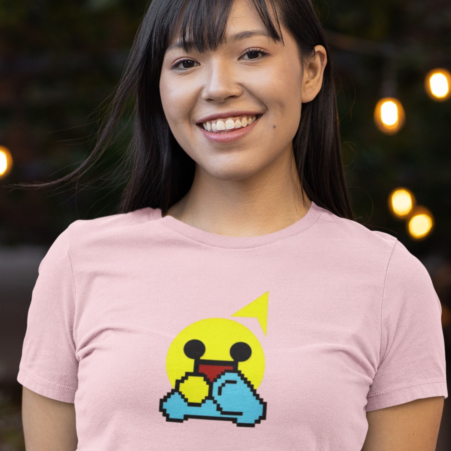 Person wearing a pink t-shirt with a pixelated character design, blurred lights in the background.