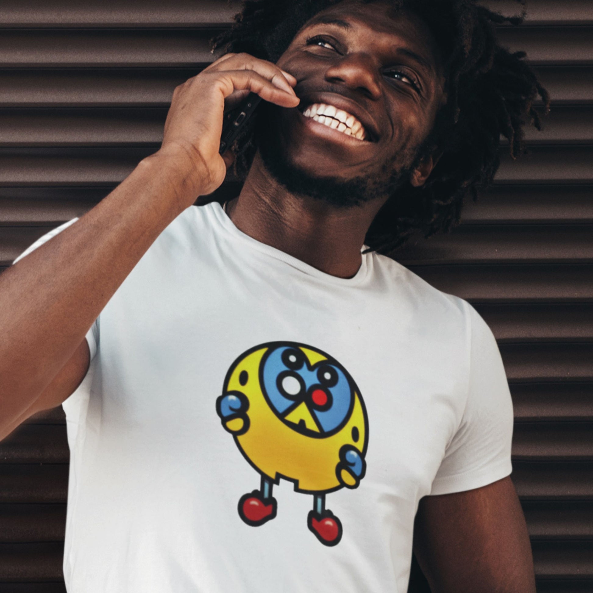 Smiling man wearing a white t-shirt with a fun, colorful cartoon illustration on a brown background.