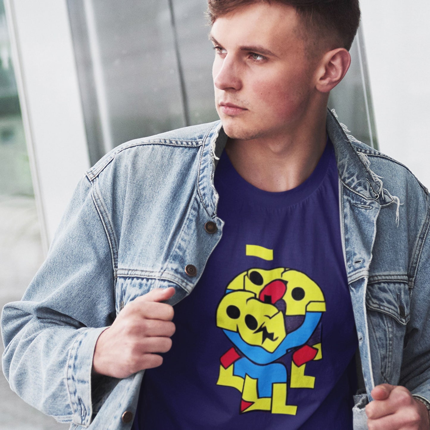 Man wearing a denim jacket over a blue t-shirt with a colorful graphic design.