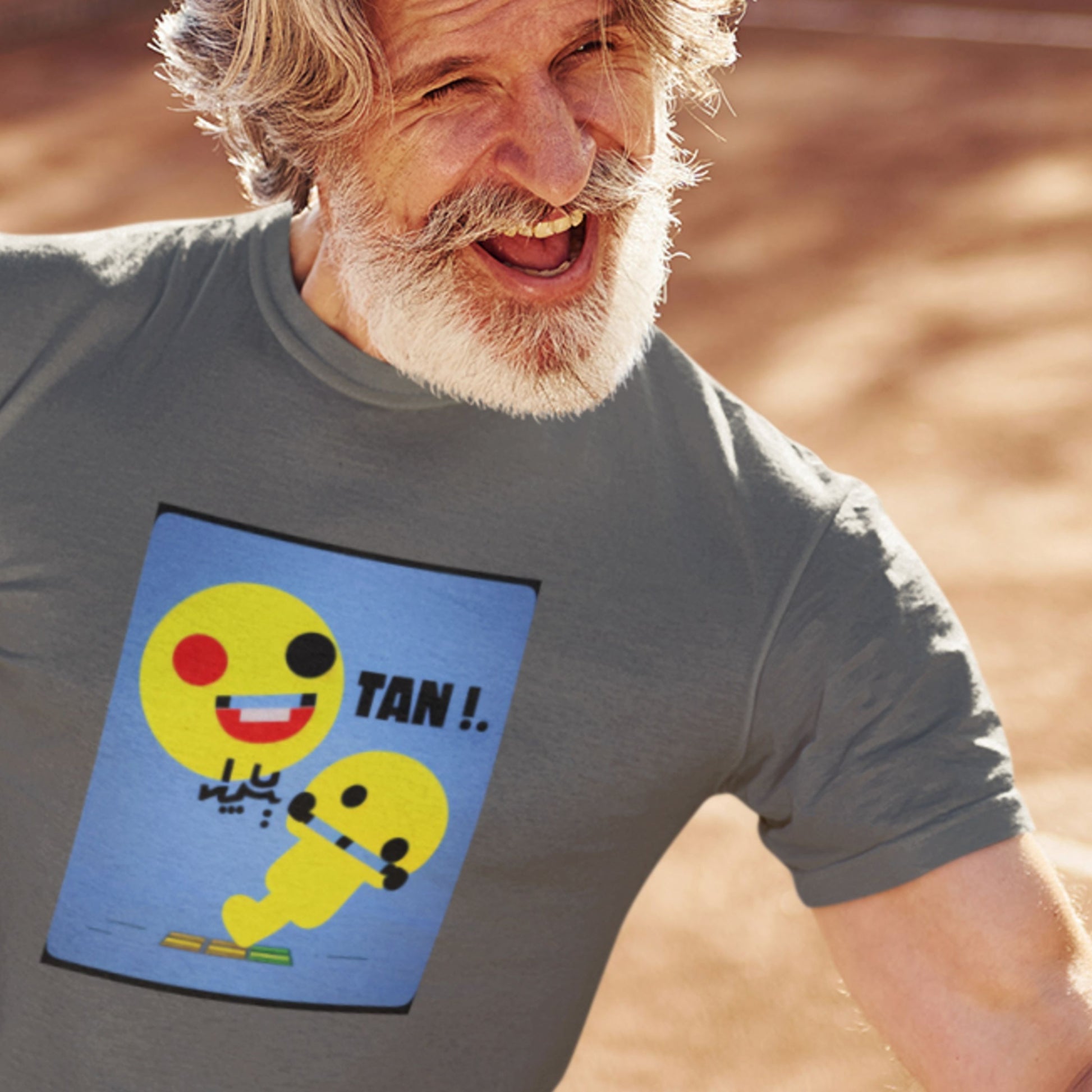 Man wearing a t-shirt with a smiley face design and 'TAN!' text, standing outdoors.