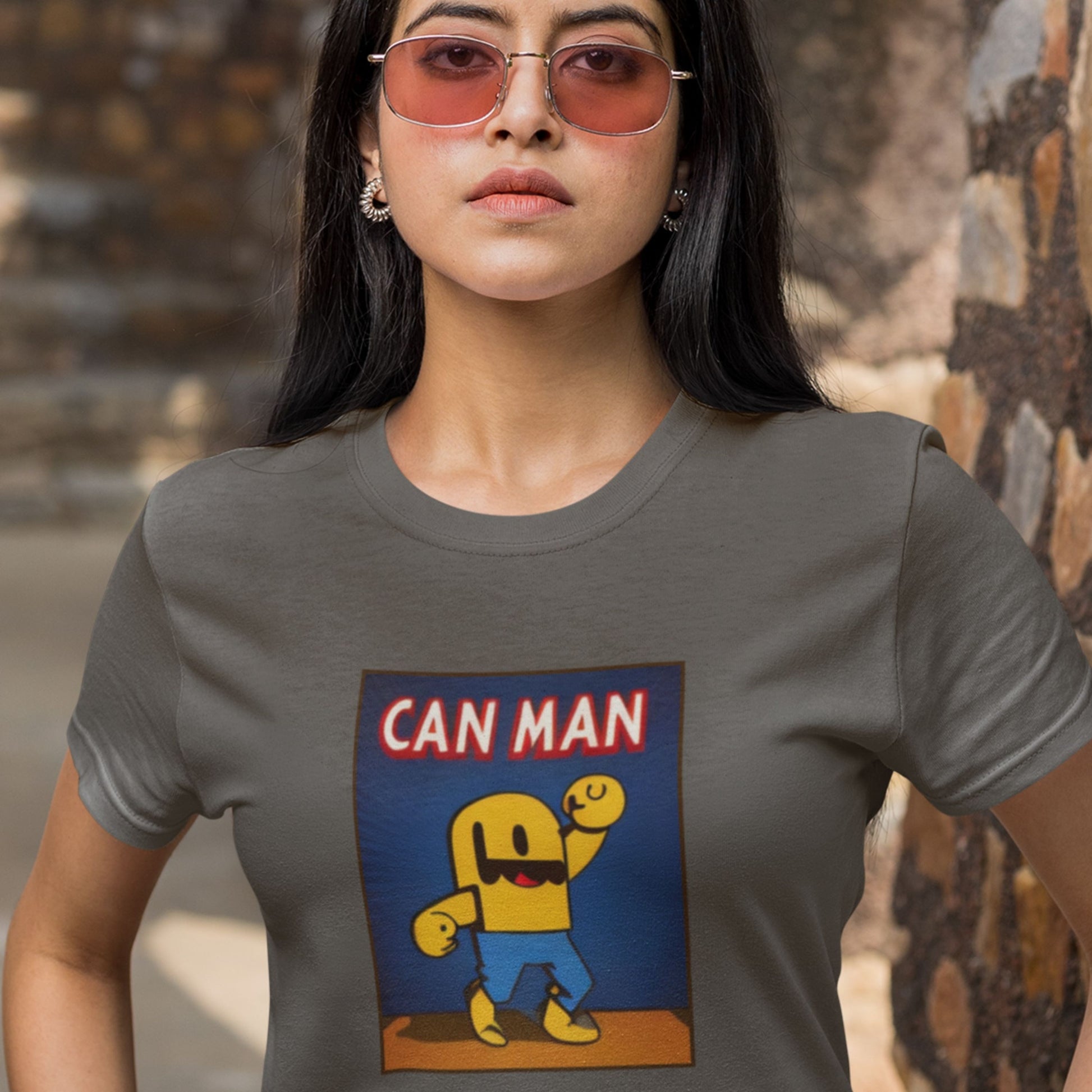 Sunglasses woman wearing a dark grey t-shirt with a fun, colorful Can Man cartoon illustration outdoors.