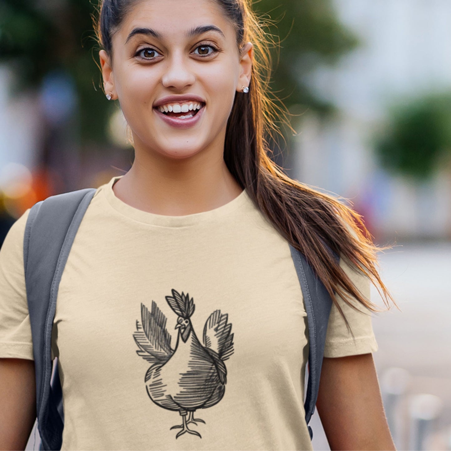 Woman wearing a beige t-shirt with a rooster design, smiling outdoors.