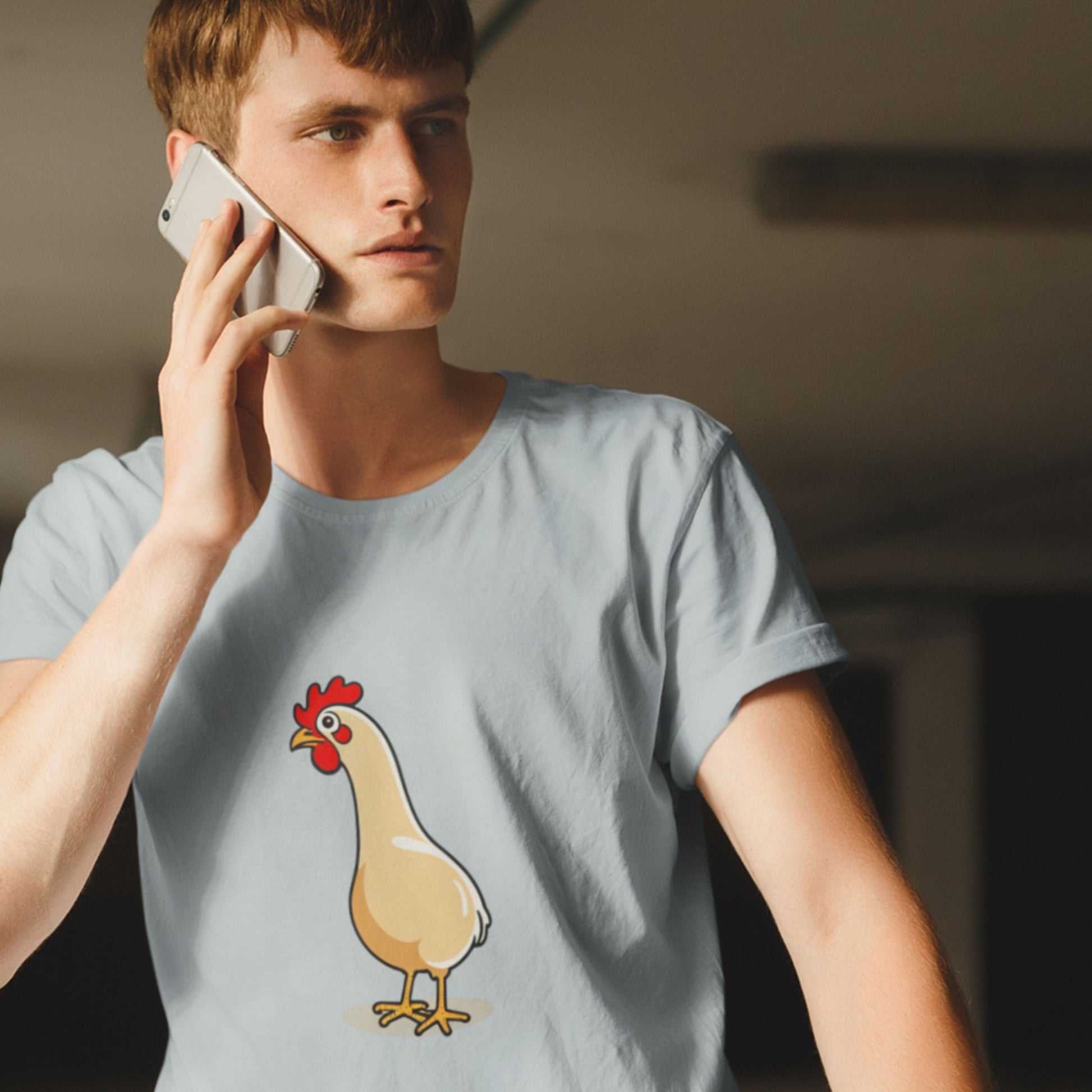 Man on the phone wearing a light grey shirt with an illustration of a rooster in a parking garage.