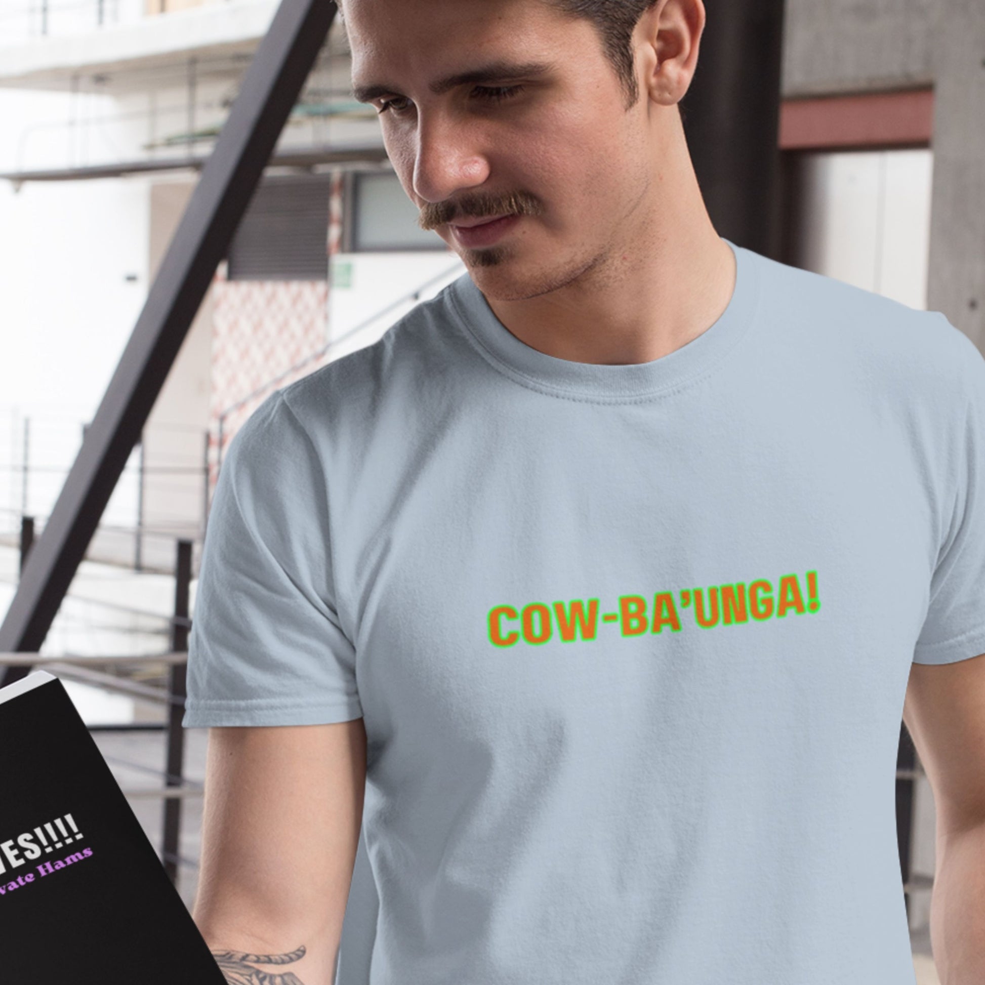 Man wearing a light blue t-shirt with 'COW-BA'UNGA!' text, standing indoors.