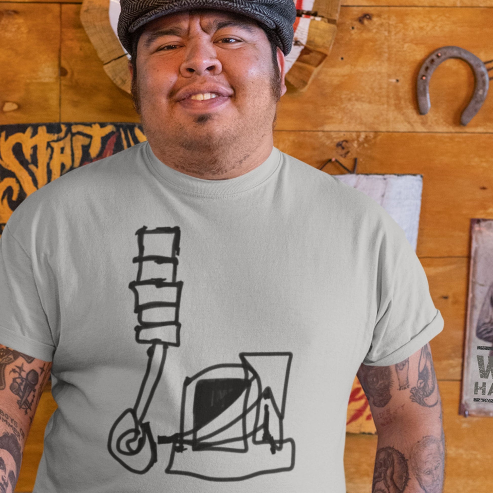 Man wearing a gray t-shirt with a black and white design, standing in front of a wooden wall with various decorations.