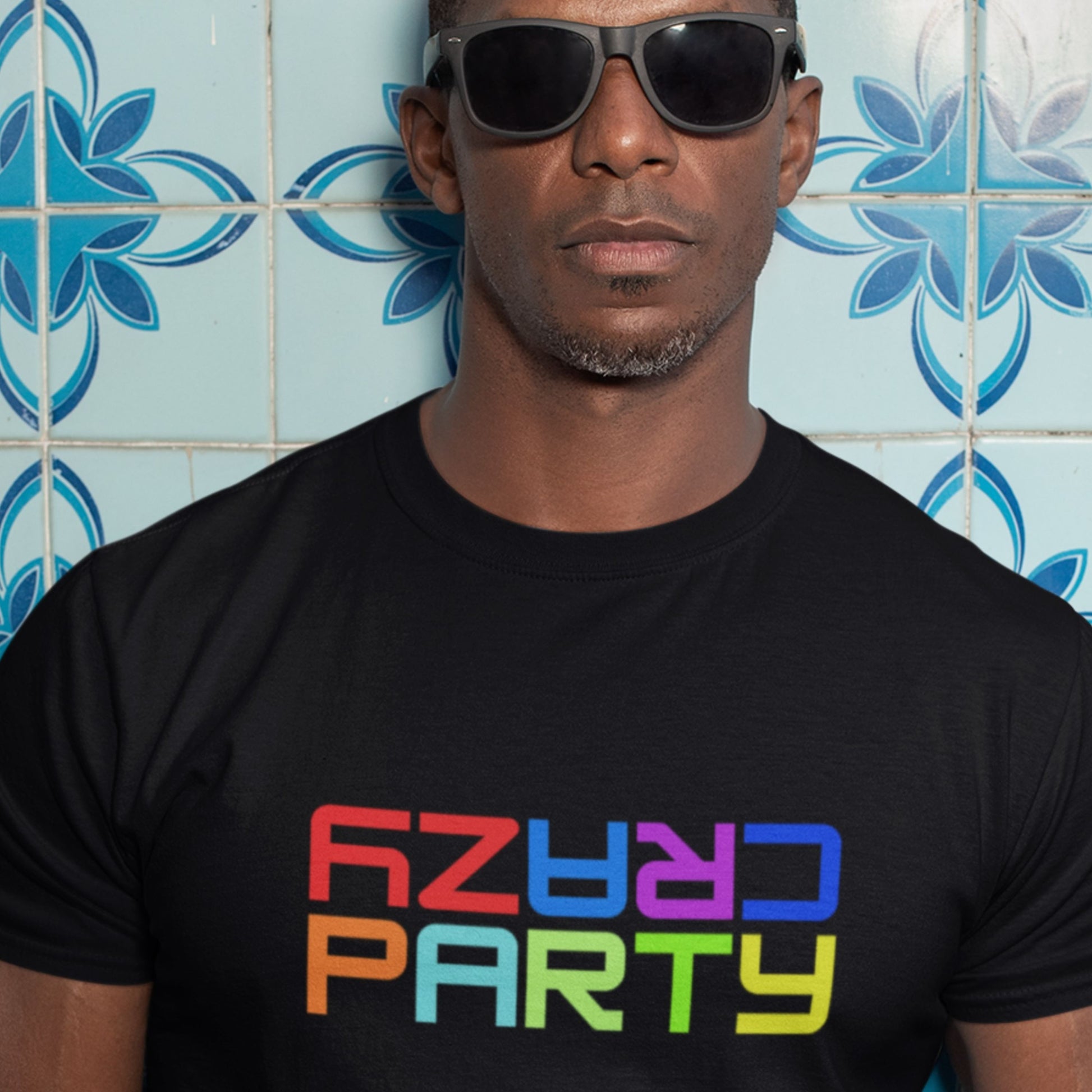 Man wearing a black t-shirt with colorful text in front of a blue tiled wall.