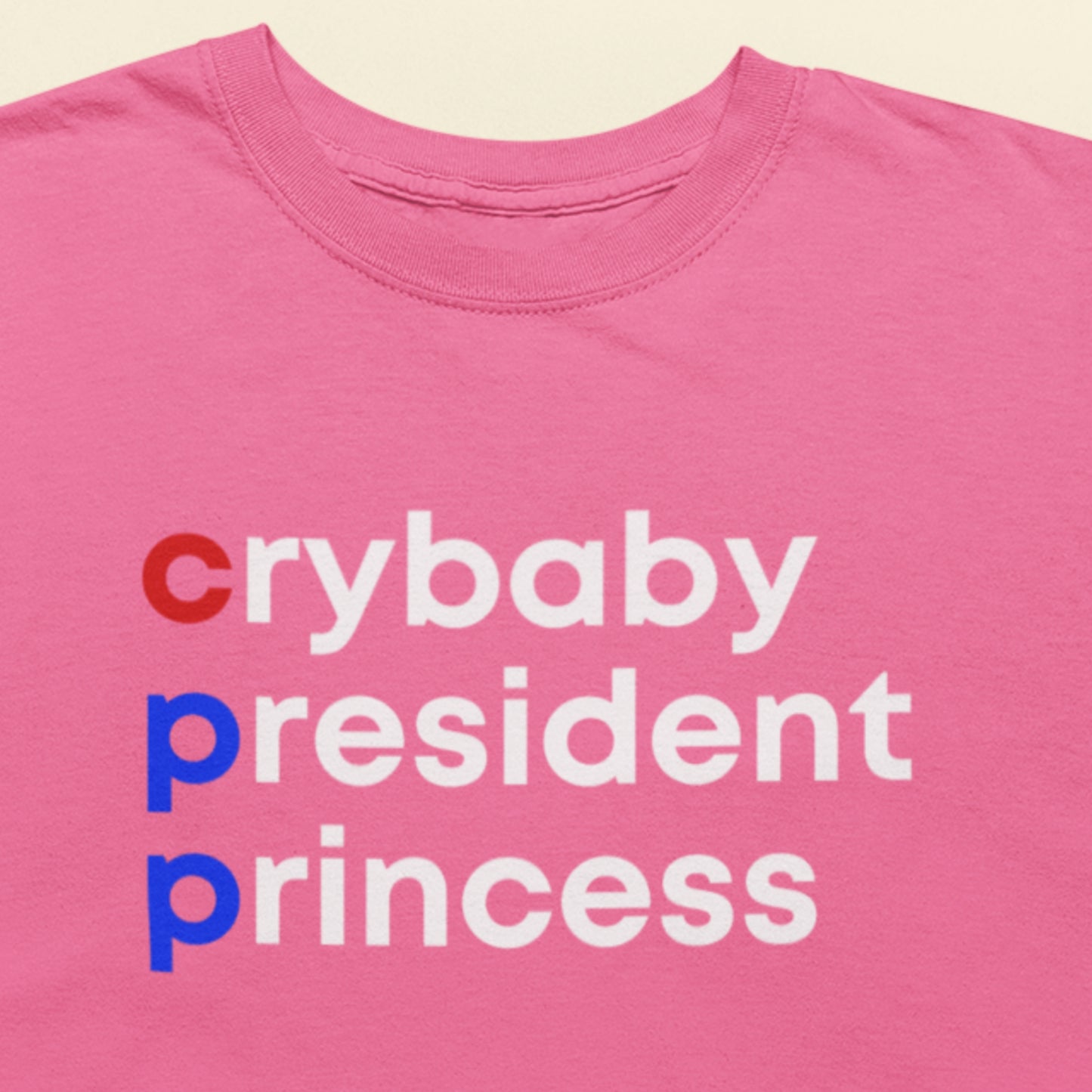 Pink t-shirt with text 'crybaby president princess' on a beige background