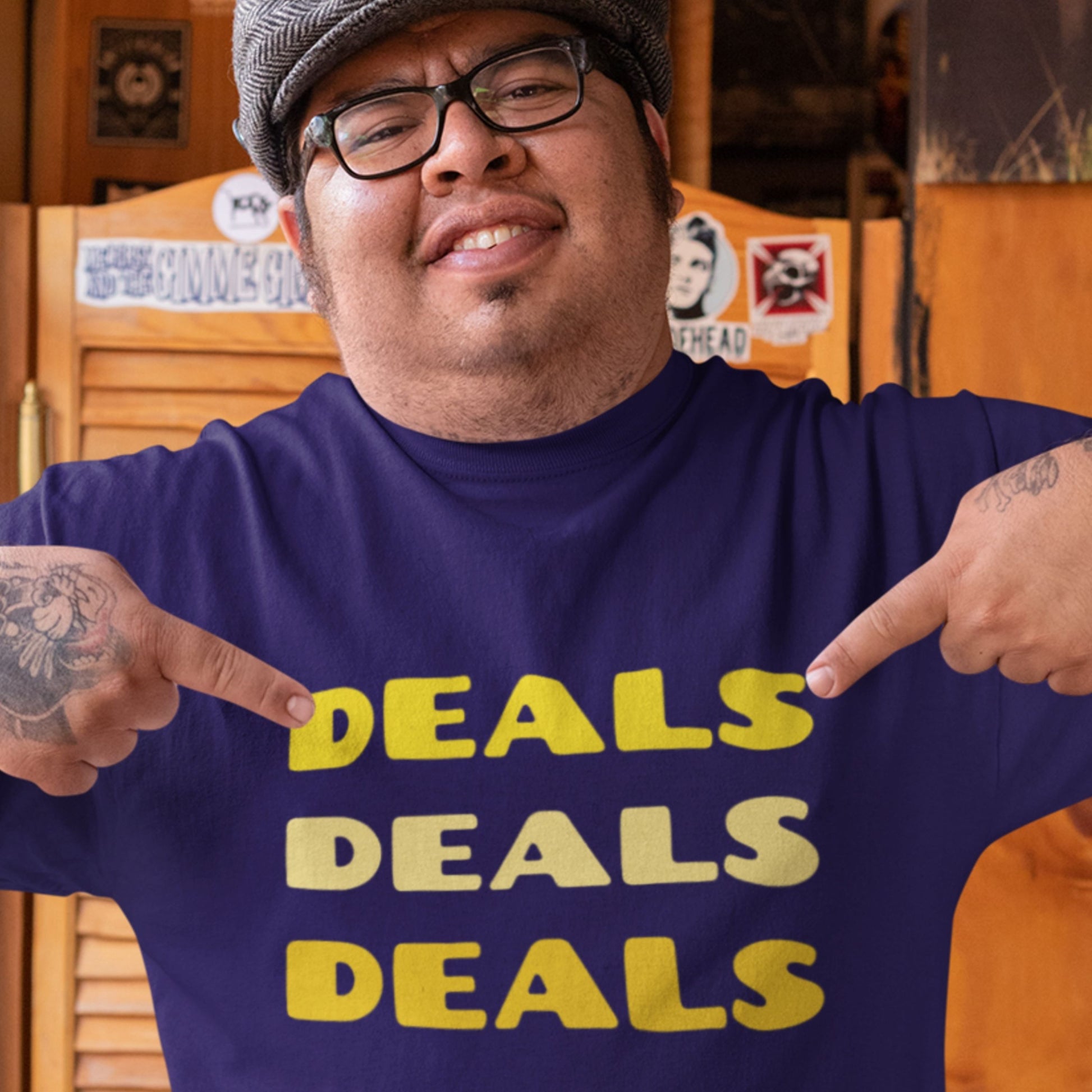 Man wearing a purple shirt with 'DEALS DEALS DEALS' text, pointing at himself.