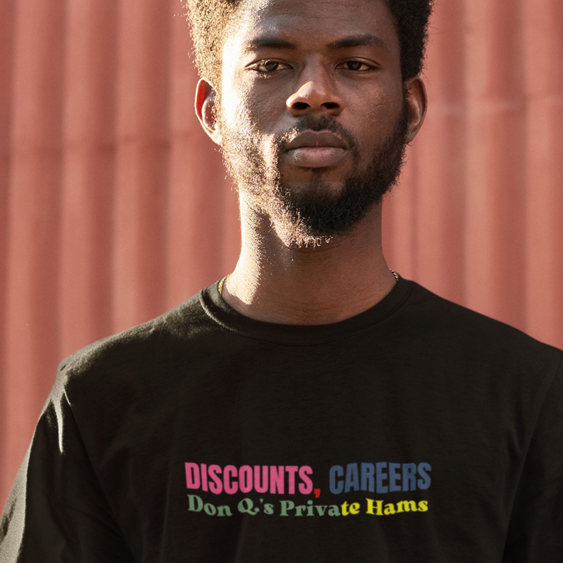 Man wearing a black t-shirt with colorful text against a red wall.
