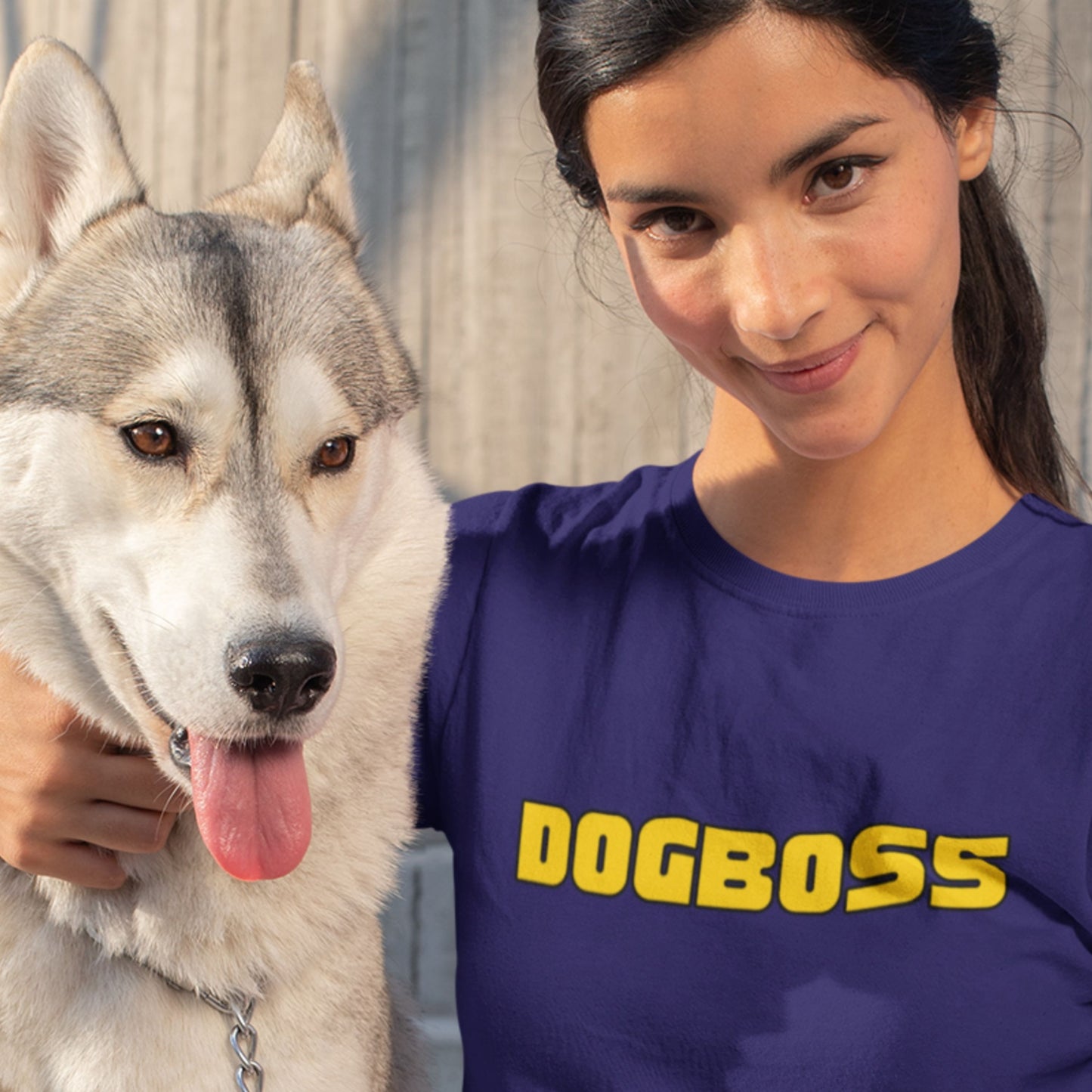 Woman wearing a purple 'DOGBOSS' shirt next to a husky dog.