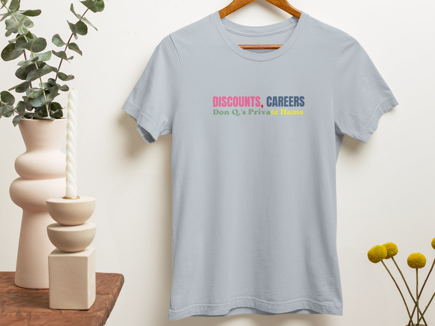 Light blue t-shirt with colorful text on a hanger against a neutral wall.