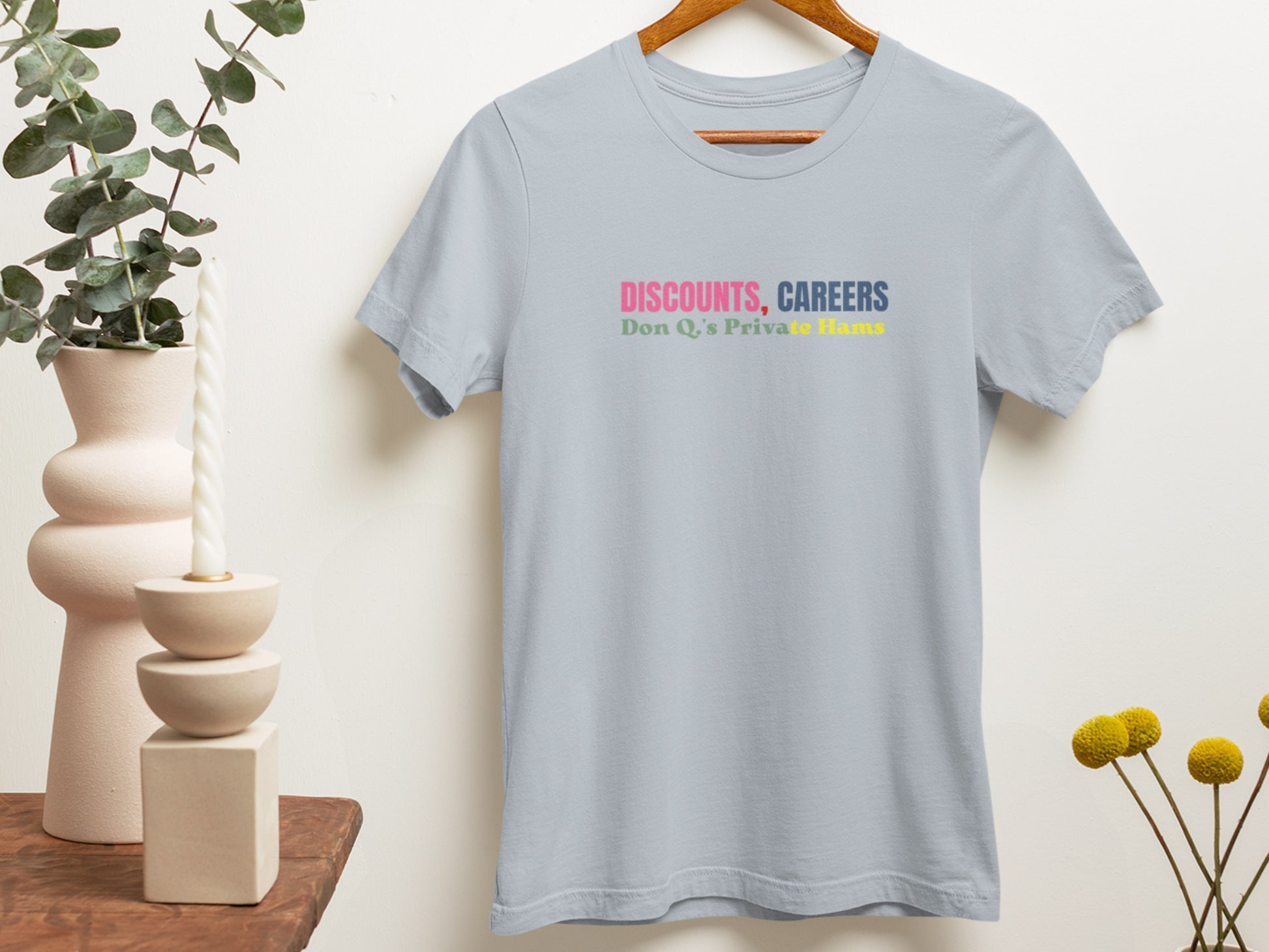 Light blue t-shirt with colorful text on a hanger against a neutral wall.
