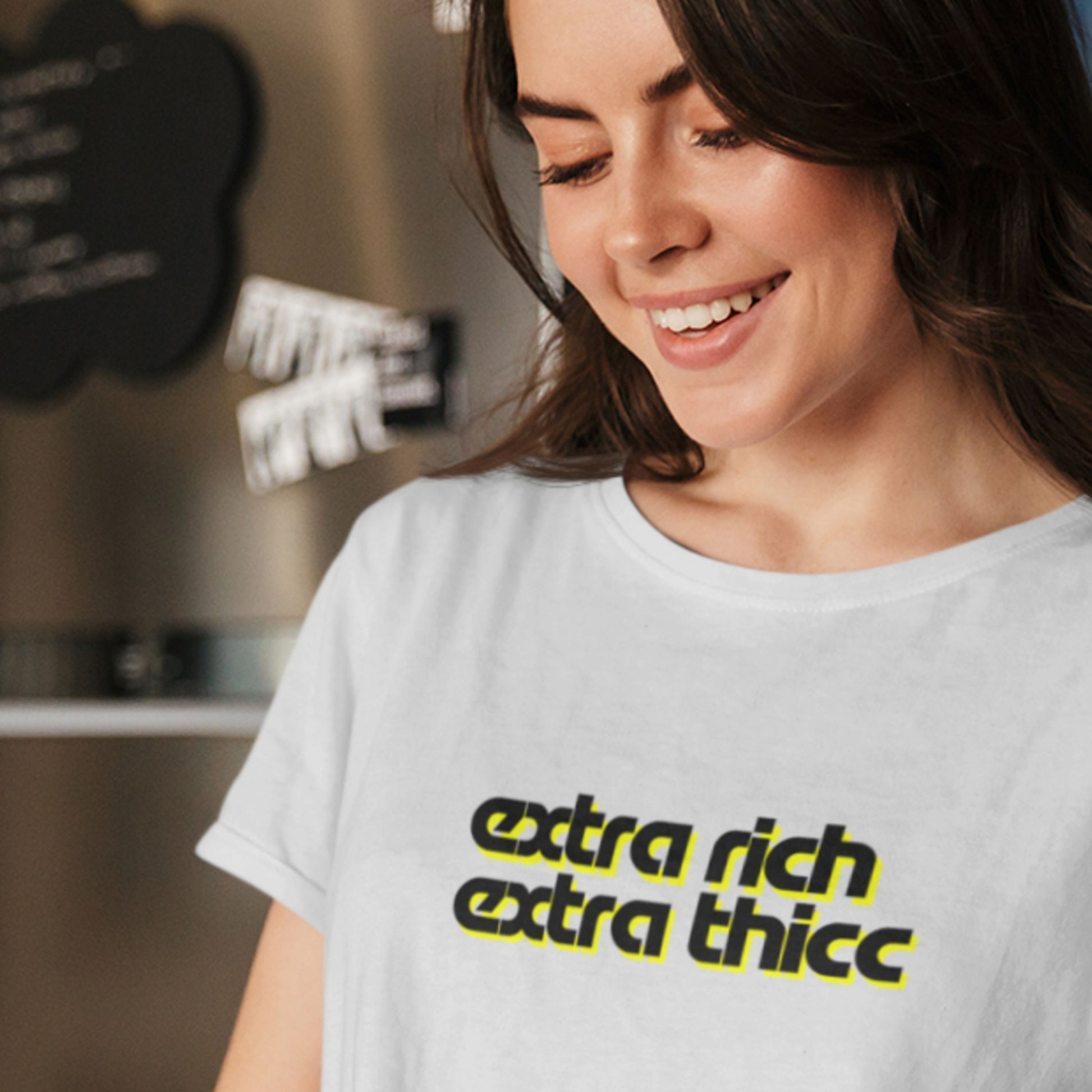 Woman wearing a light grey t-shirt with 'extra rich extra thicc' text in a casual setting.