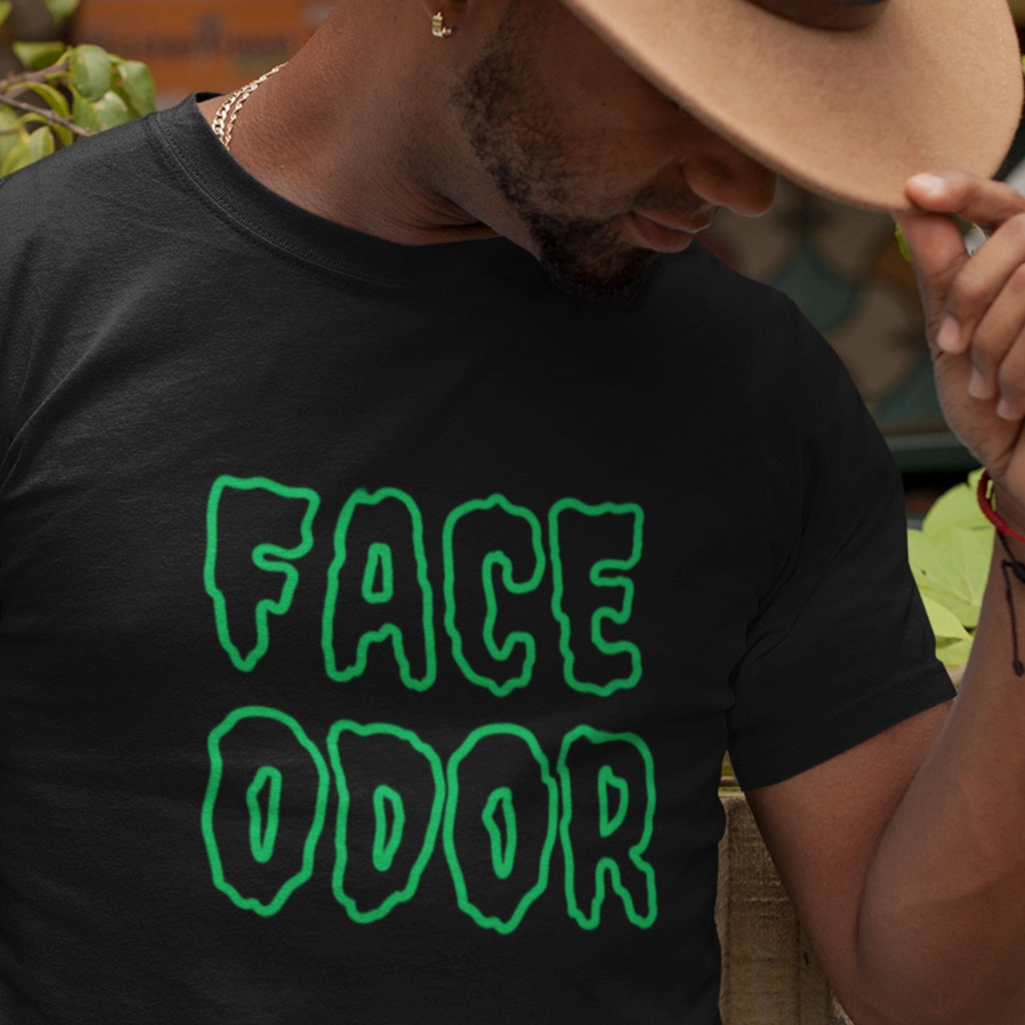 Person wearing a black t-shirt with 'FACE ODOR' in green text, outdoors.