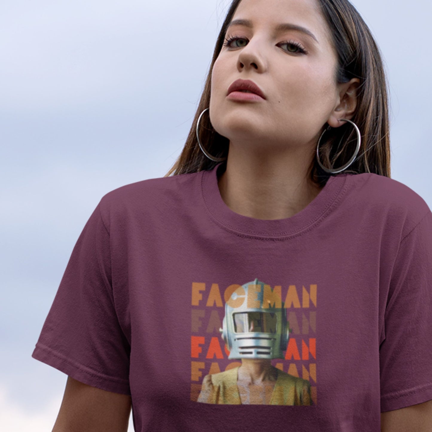 Woman wearing a maroon t-shirt with a graphic design and text against a clear blue sky.